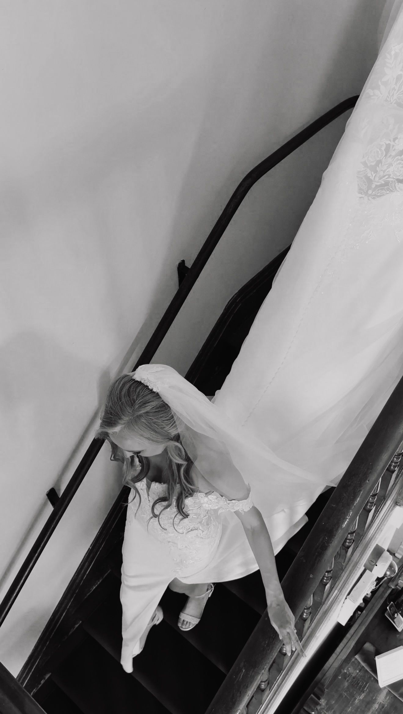 Black and white overhead view of a bride in a white wedding dress and veil descending a staircase.