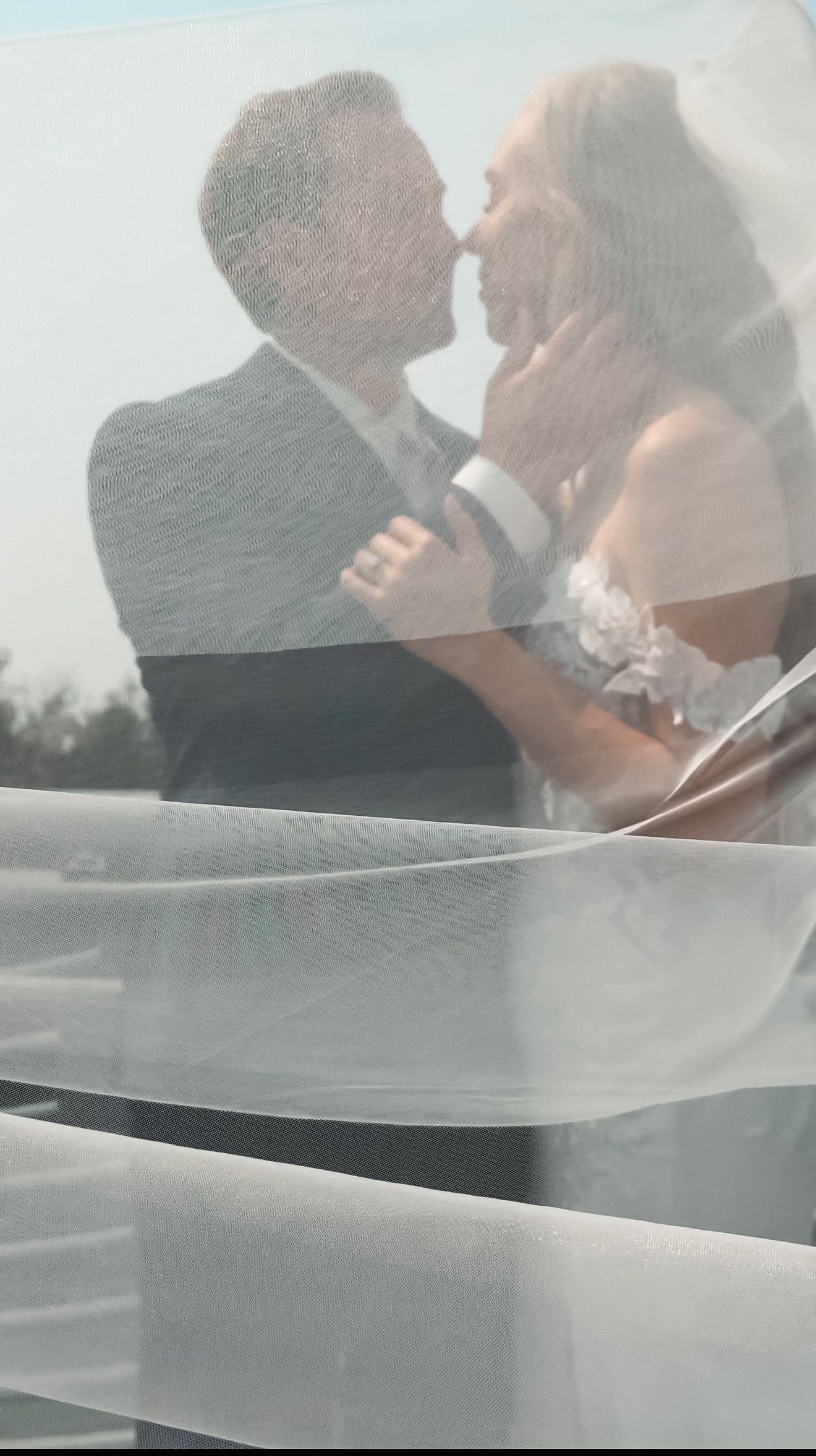 Dreamy double exposure wedding photo of bride and groom kissing, captured through the brides flowing white veil.