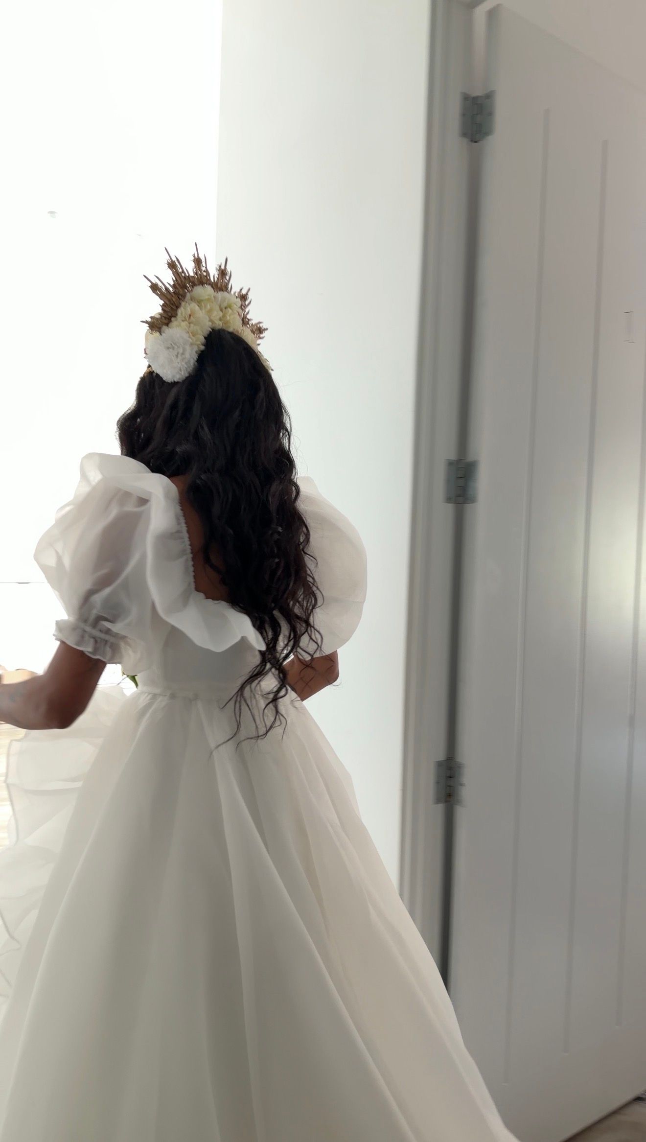 Bride in white ball gown with puff sleeves and floral crown viewed from behind.