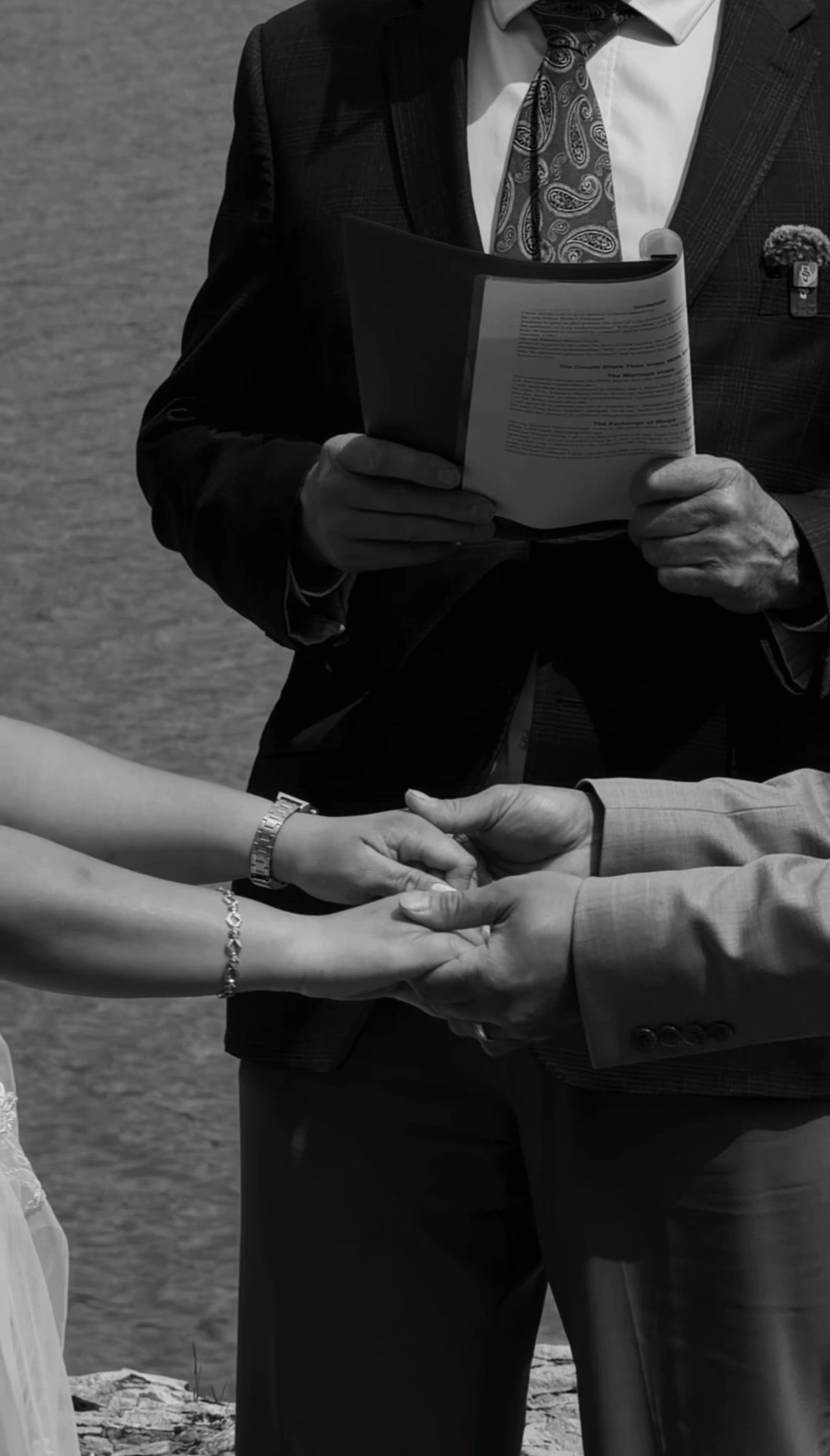 Black and white close-up of couple exchanging vows and holding hands during wedding ceremony with officiant.