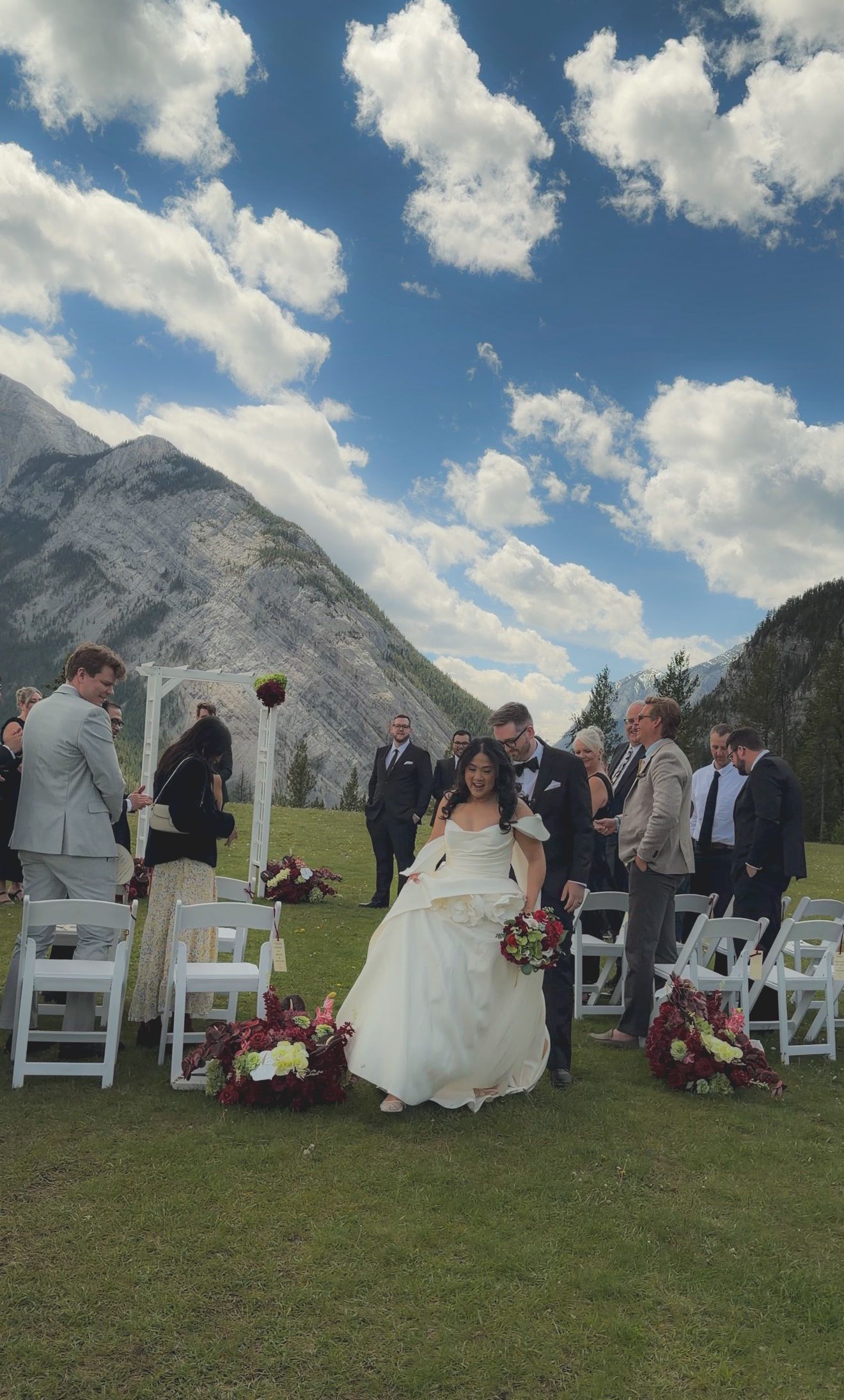 Bride walks down the aisle at an outdoor mountain wedding ceremony in Banff with white chairs and floral arrangements.