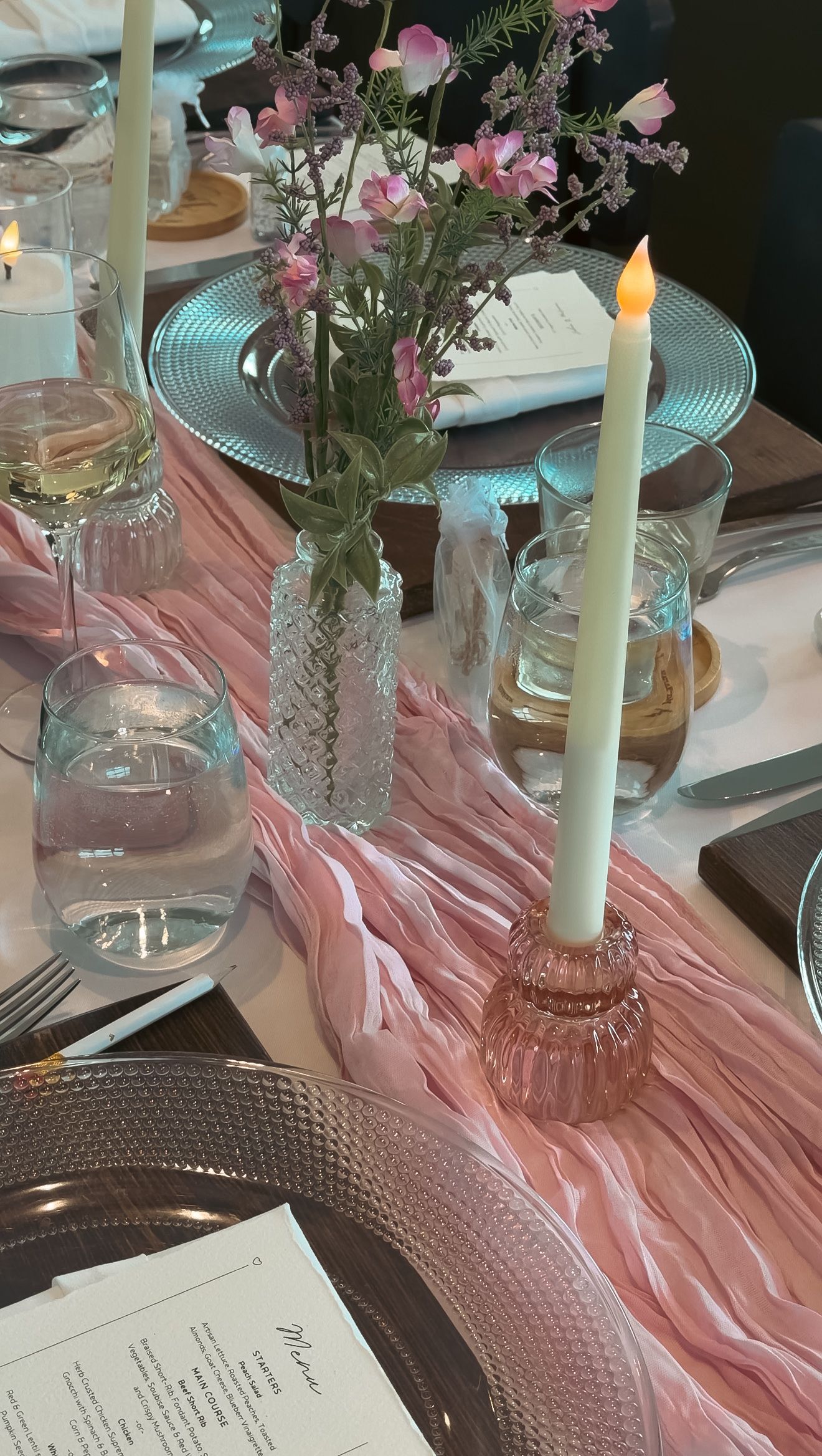 Elegant wedding reception table with pink chiffon runner, lit taper candle, and delicate floral centerpieces.