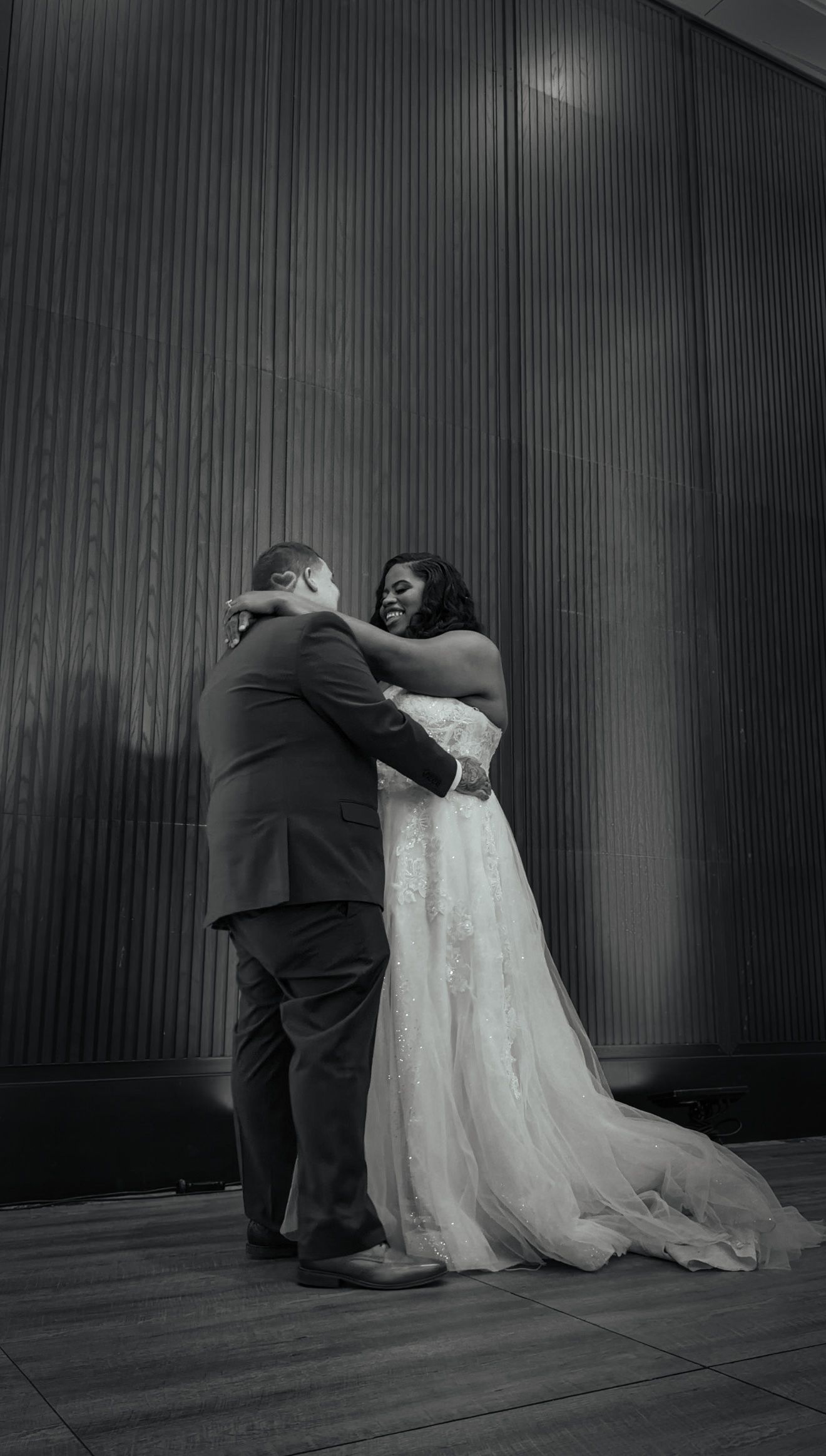 Newlywed couple shares a joyful first dance embrace in a black and white wedding reception photo.