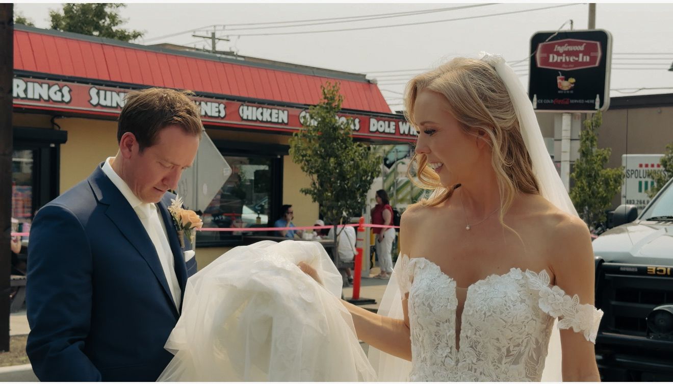 Bride and groom in wedding attire outside a fast food restaurant, groom holding bride's dress train.