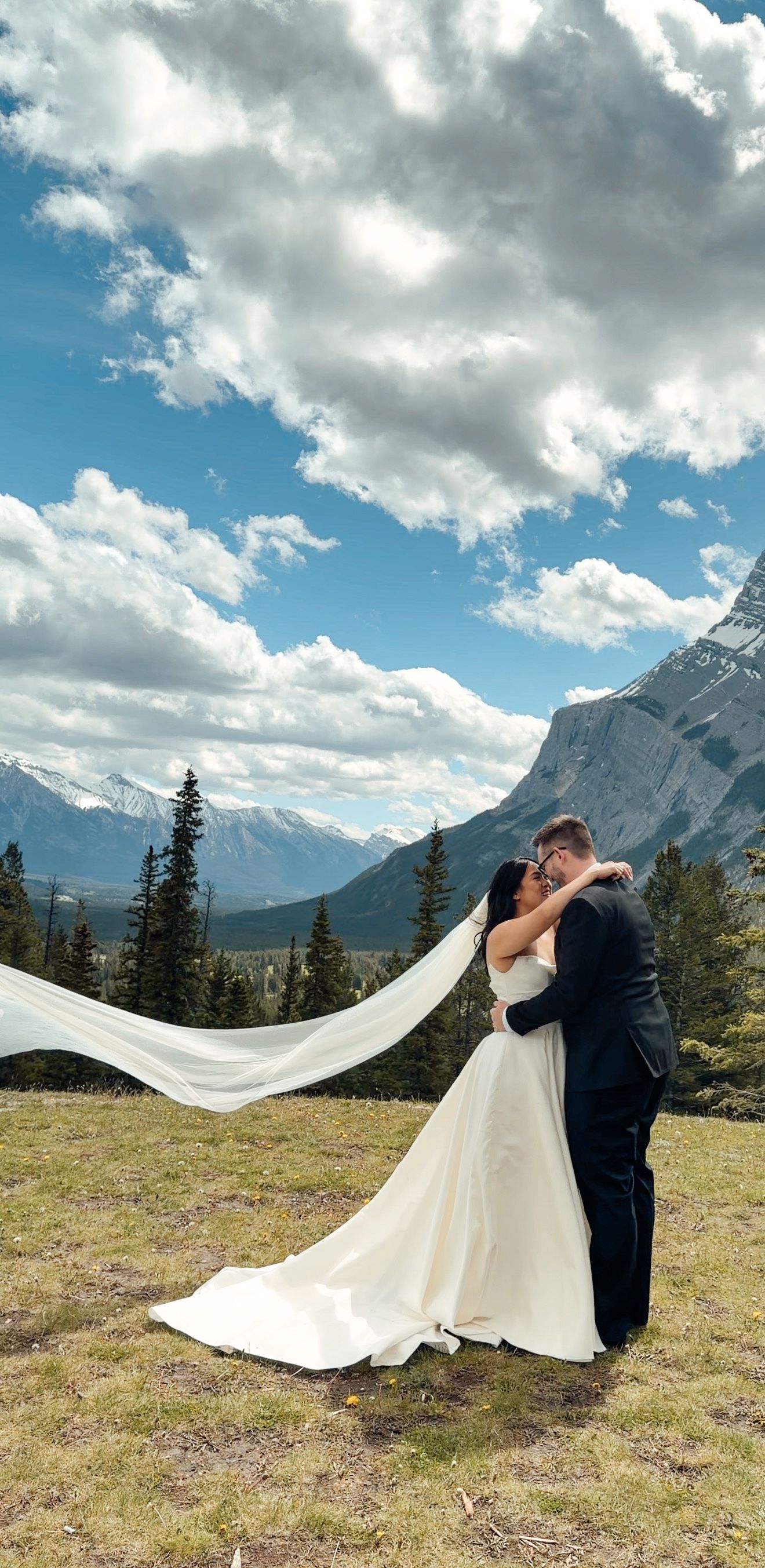 Bride and groom kissing with veil flowing in wind against stunning Rocky Mountain backdrop.
