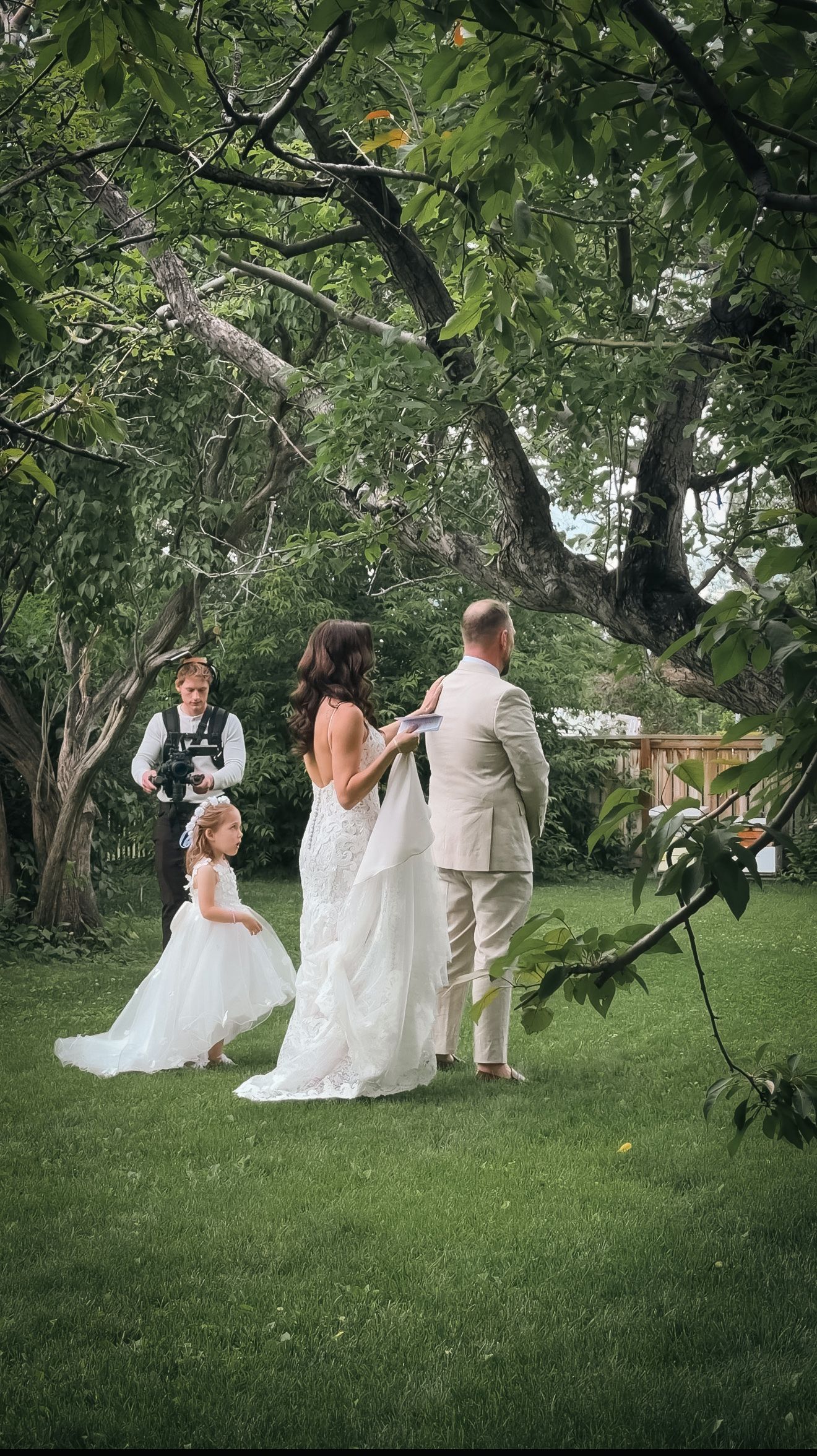 Bride and groom exchange vows under trees as flower girl and ring bearer participate in ceremony.