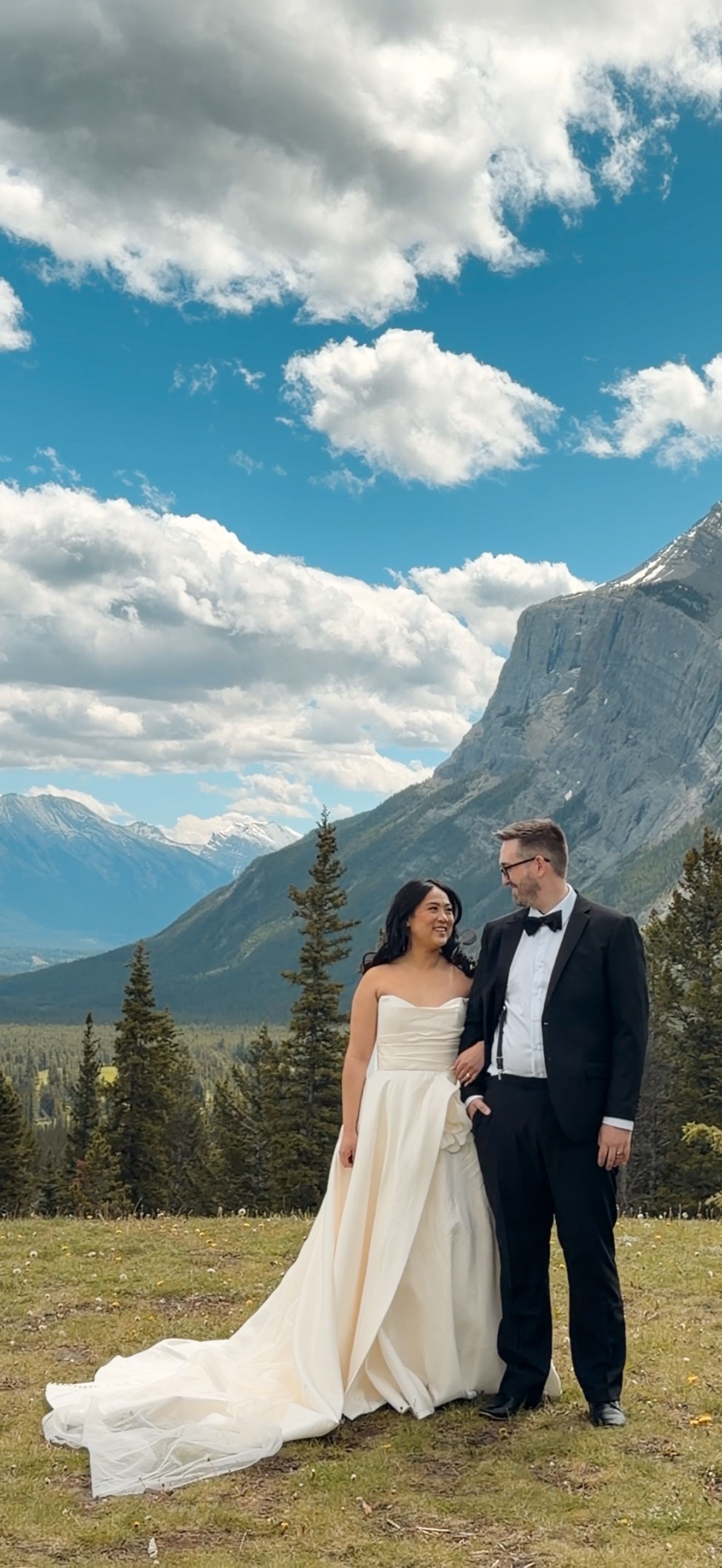 Bride and groom posing together with breathtaking Rocky Mountain landscape and blue sky in Banff, Canada.