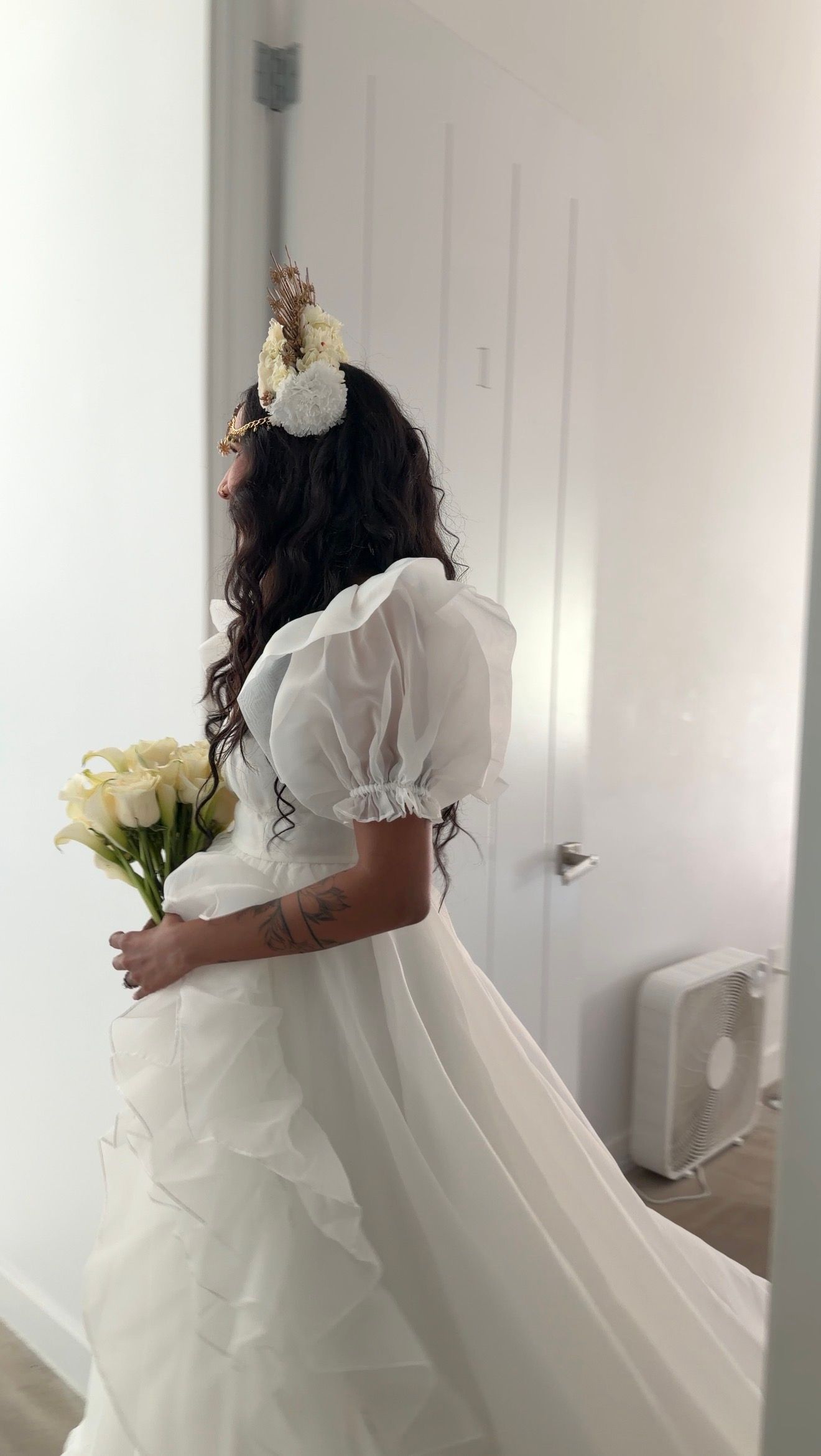 Bride in white organza puff sleeve wedding gown holding cream roses with floral crown in her hair.