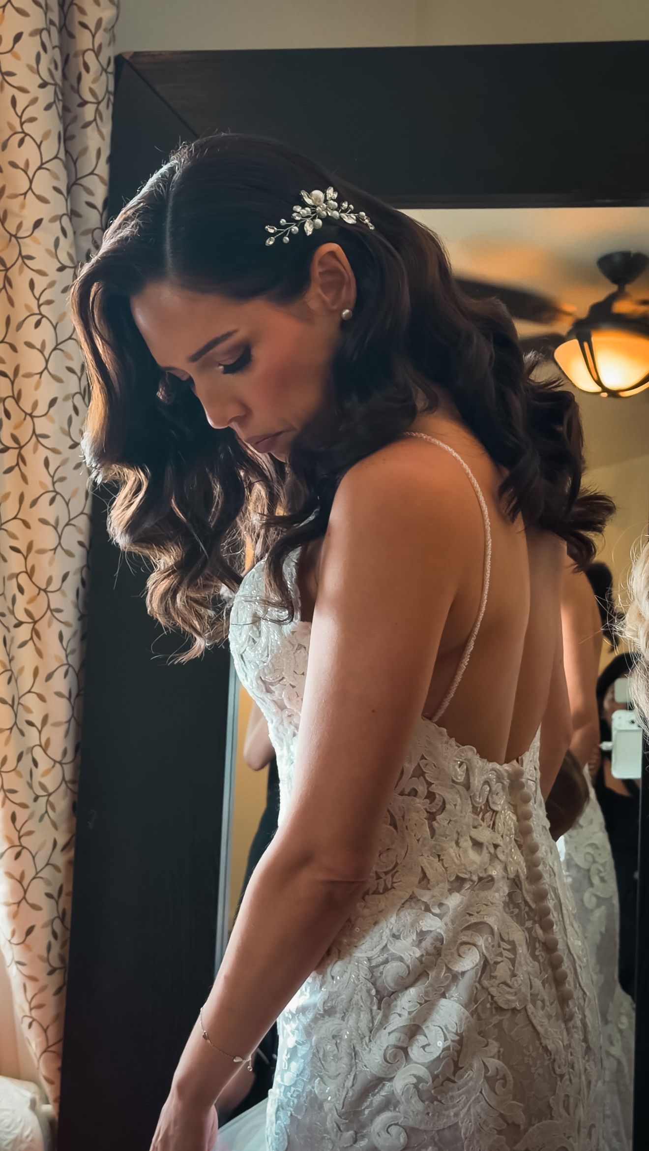 Beautiful bride in backless lace wedding gown with floral hair accessory and flowing brunette waves.