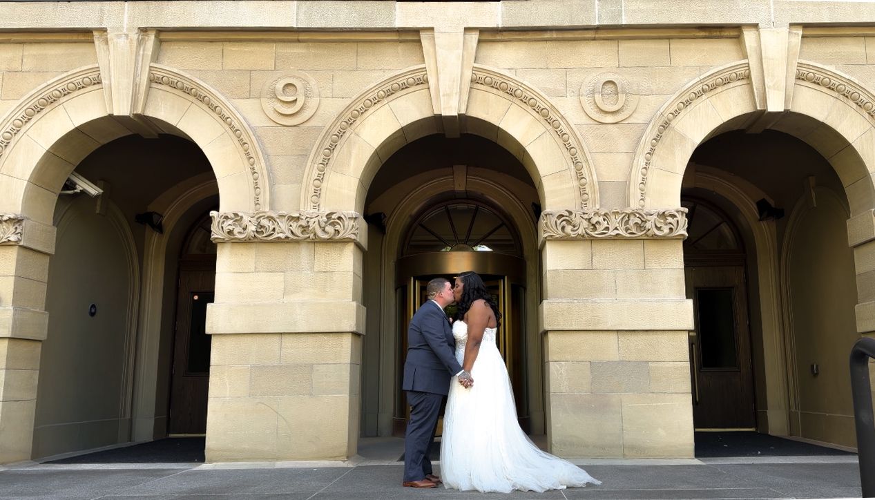 Bride and groom share a romantic moment outside an elegant stone building with arched architecture.