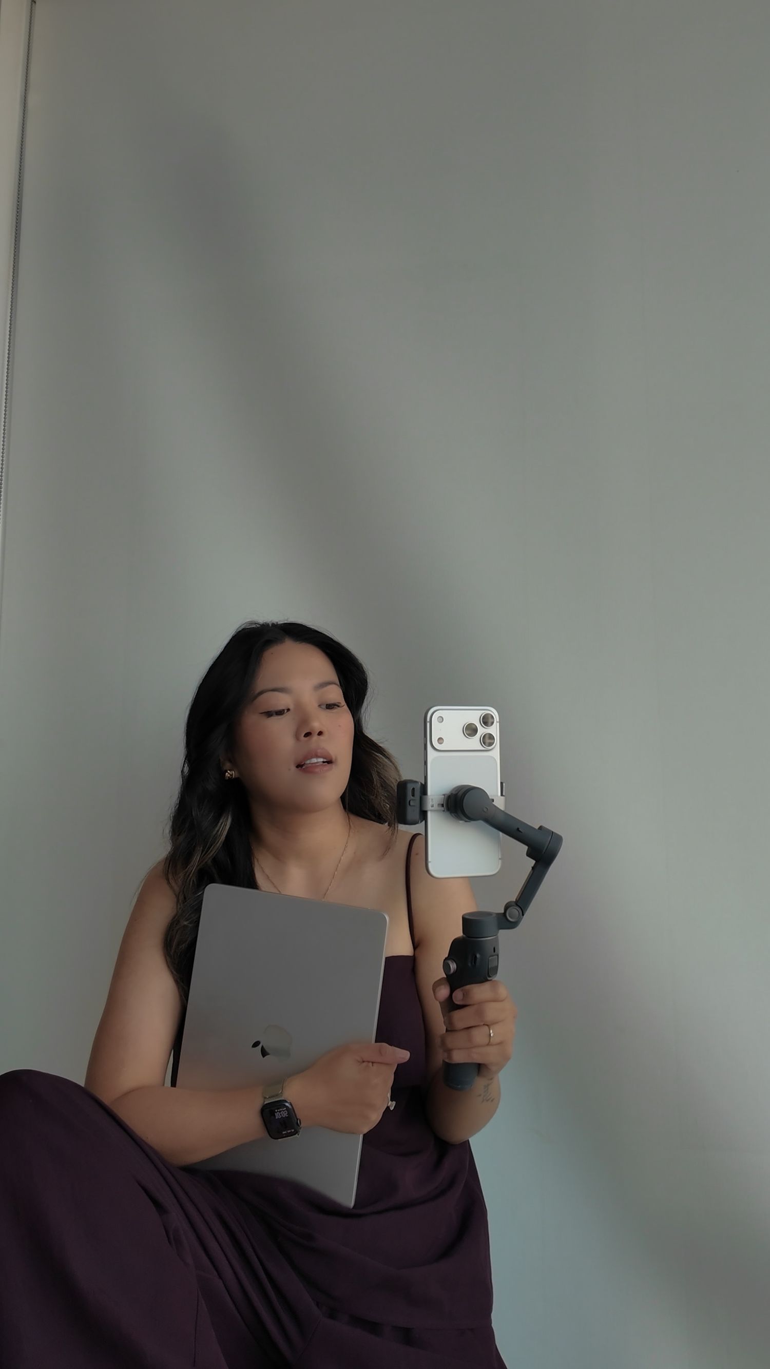 Woman in purple dress holding a laptop and smartphone on a gimbal stabilizer against a light gray background.