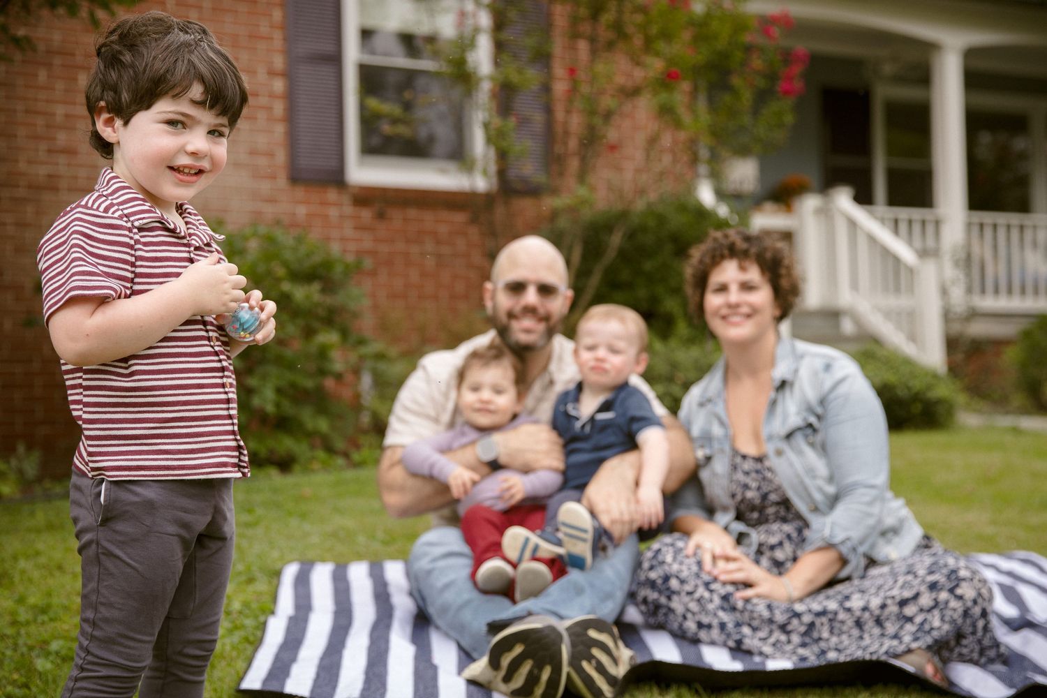 Happy family with two young children relaxes on a blanket in front of their home.