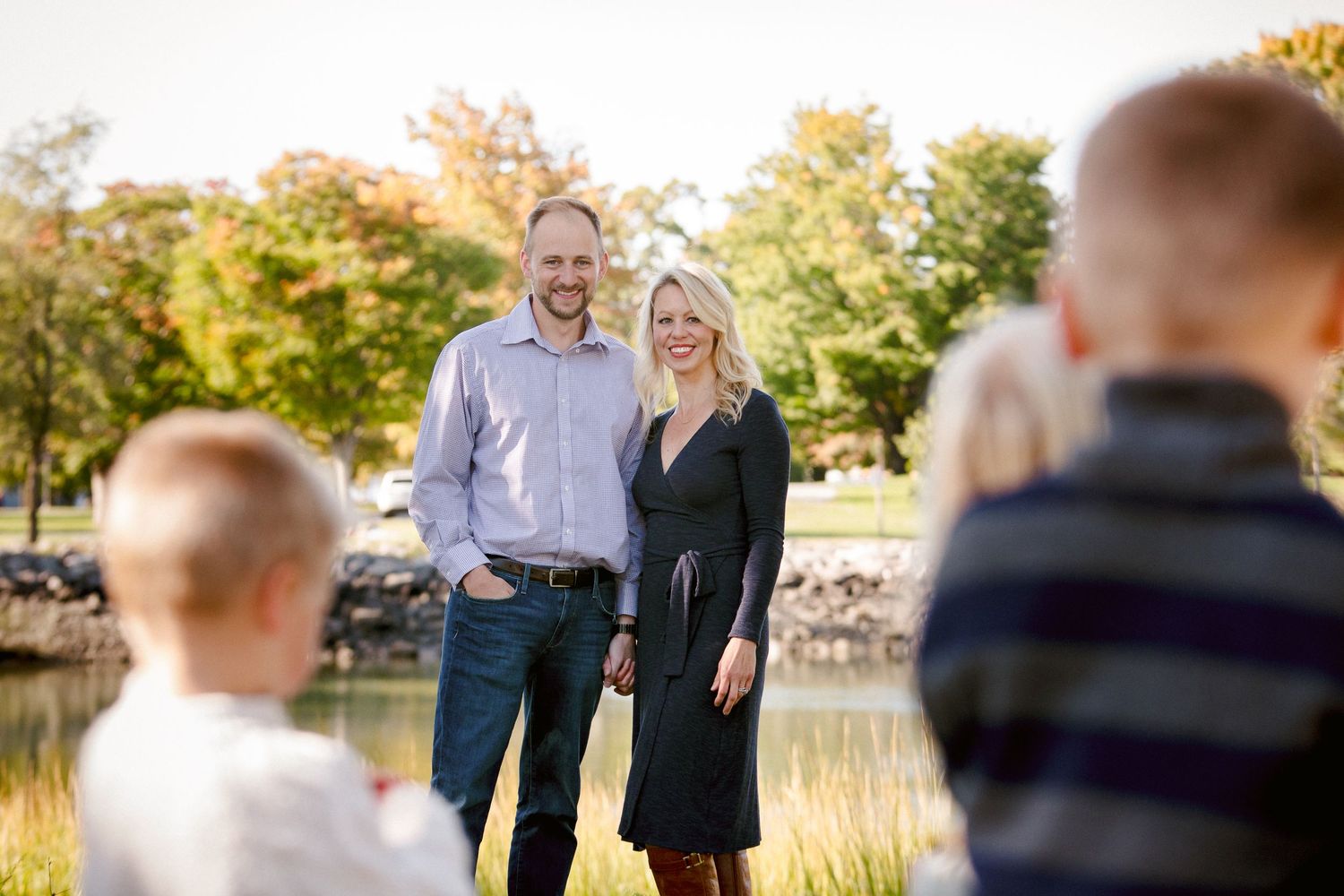 Couple posing for family portrait near pond with children in foreground blurred.
