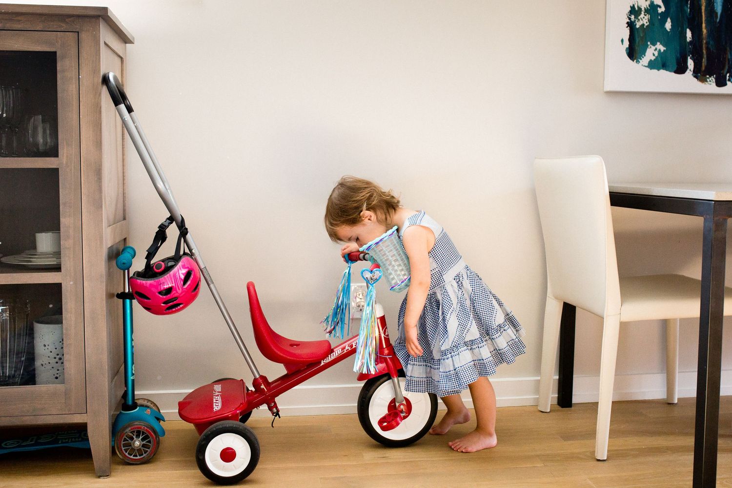 Toddler girl in blue dress playing with red Radio Flyer tricycle in modern home interior.