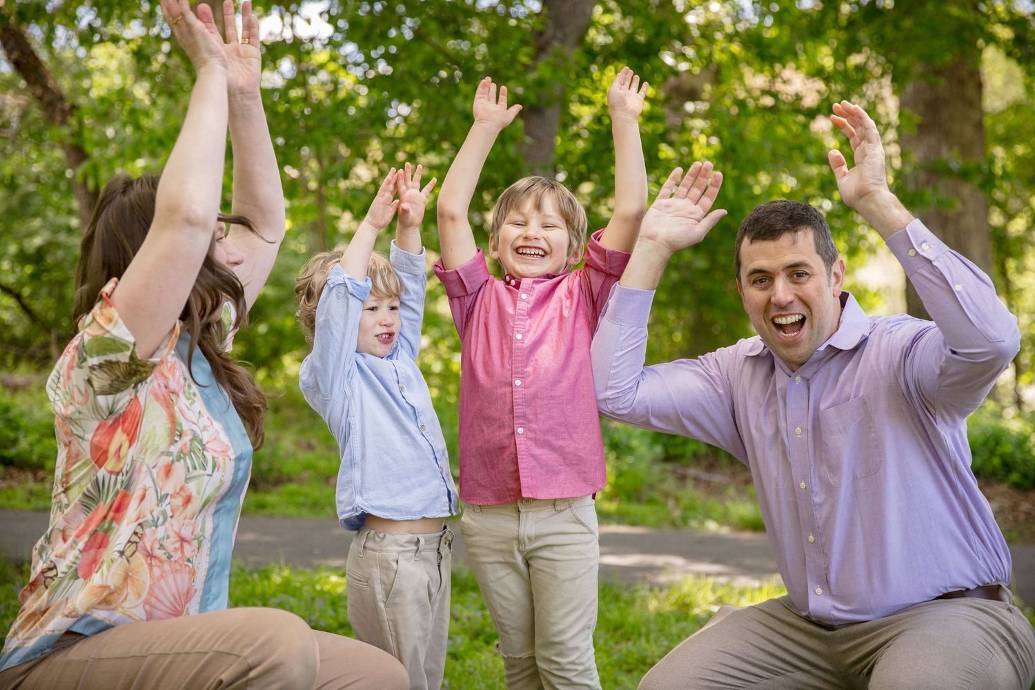 Happy family of four celebrating outdoors with raised arms, smiling in a lush green park setting.