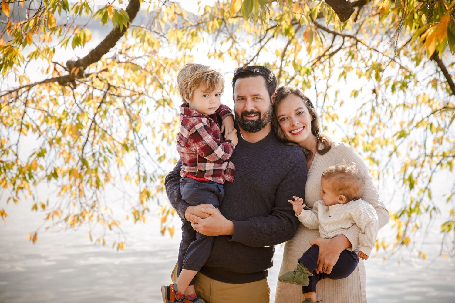 Happy family of four poses under golden autumn foliage near a lake.