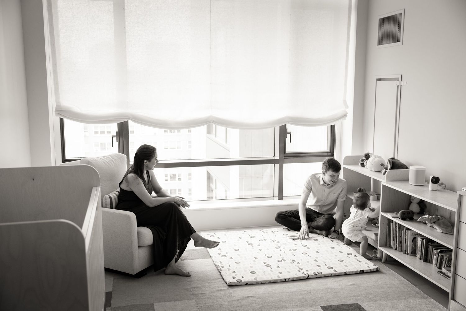Black and white family photo of parents and child relaxing together in a modern minimalist nursery room.