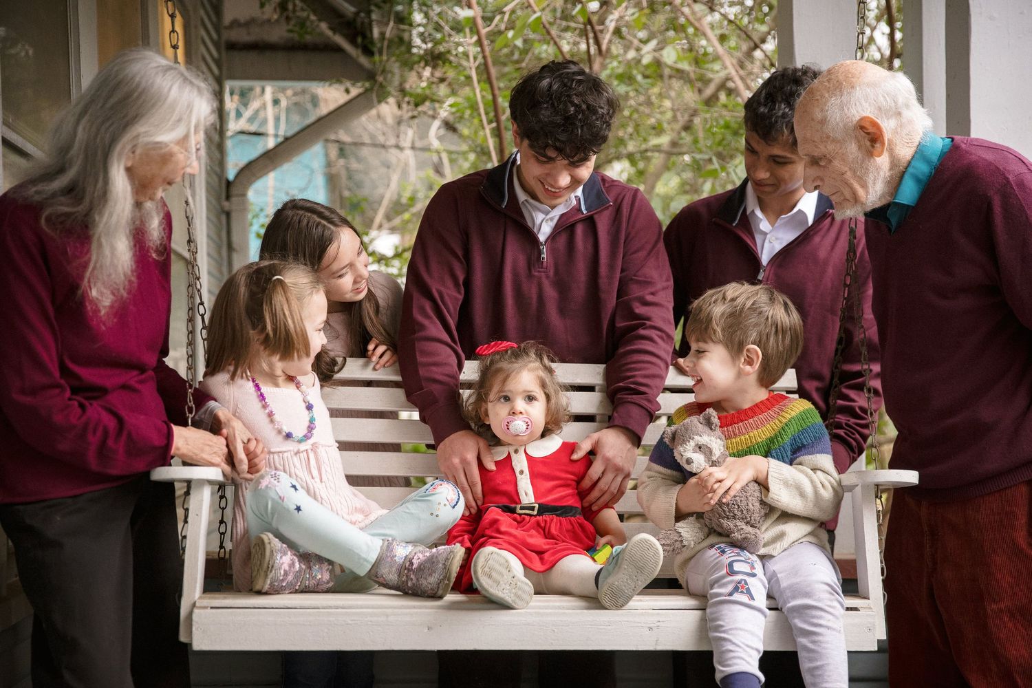 Multi-generational family gathering on a porch swing, smiling together with three young children.