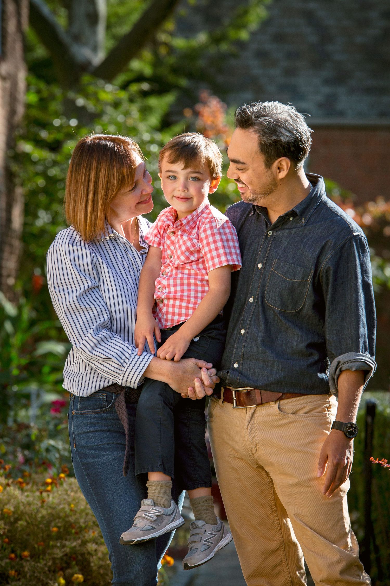 Happy family portrait with parents holding toddler son in garden setting.