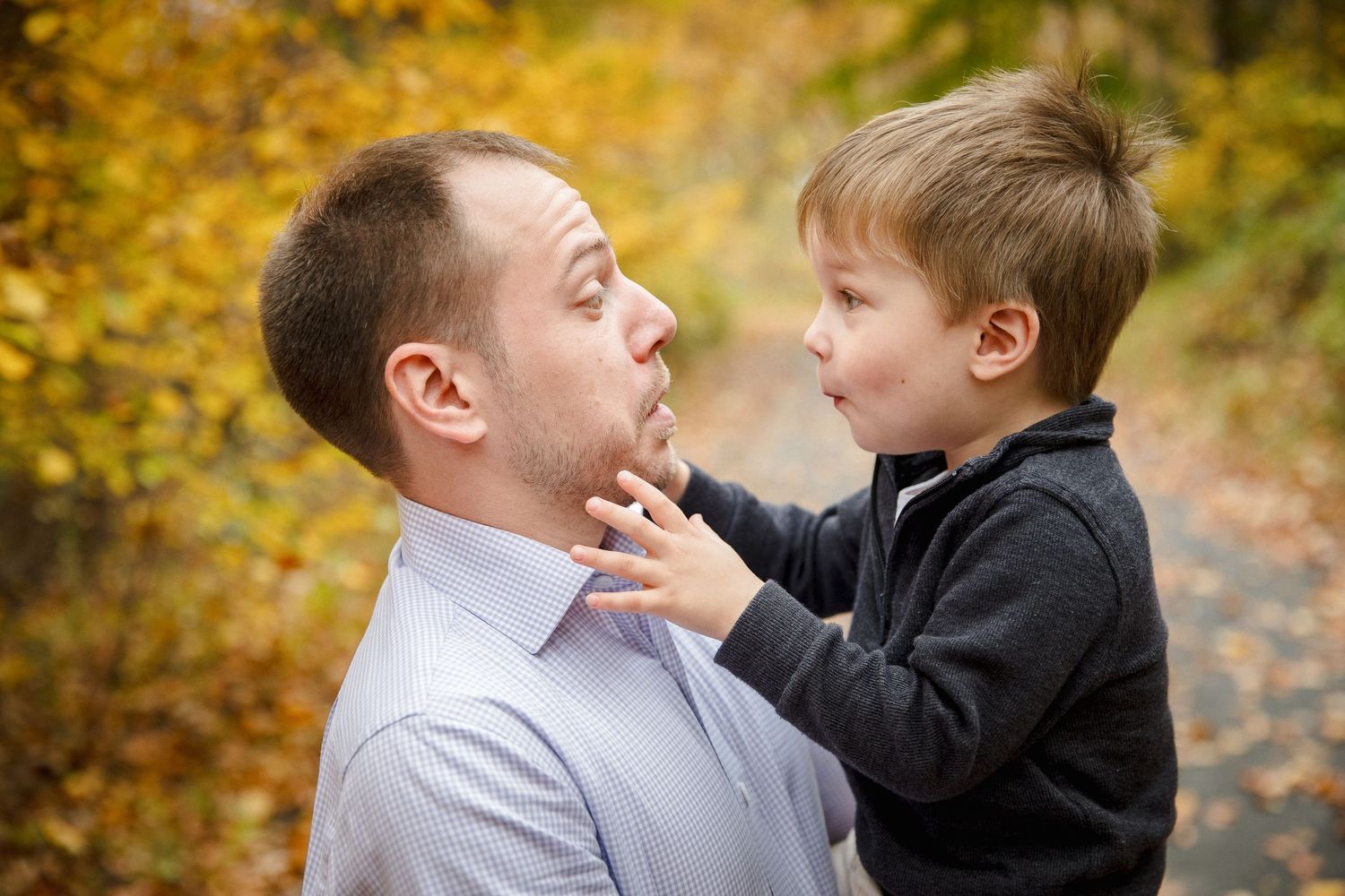 Father and young son share a playful moment outdoors during fall season.