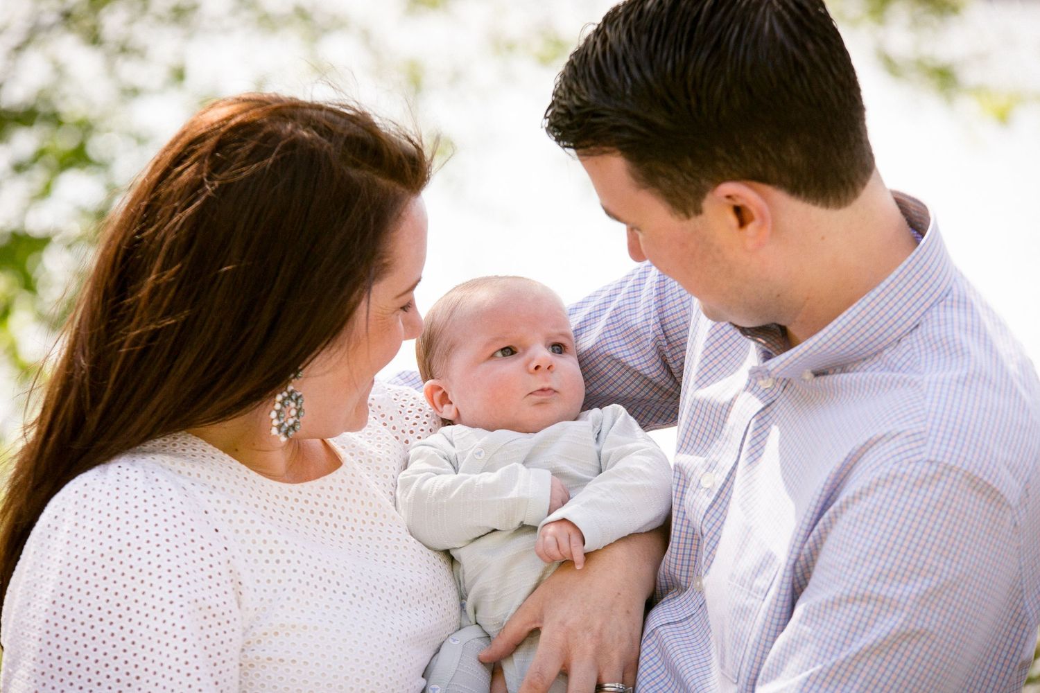 Loving parents gazing at their newborn baby held gently between them outdoors.