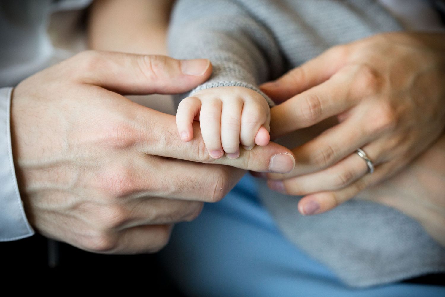 Close-up of parents gently holding their newborn babys tiny hand with wedding ring visible.