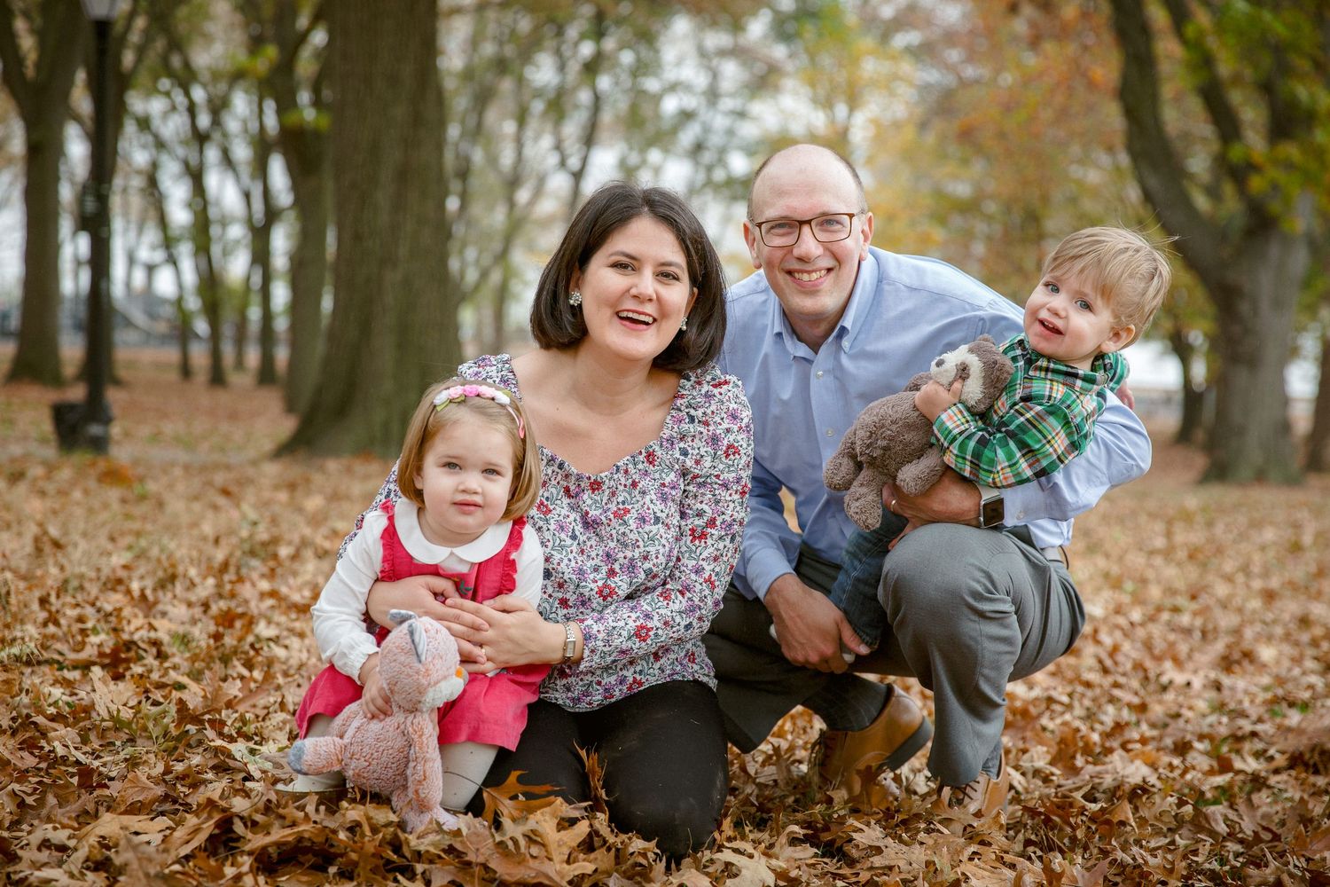 Happy family of four poses together in colorful fallen autumn leaves in a wooded park.
