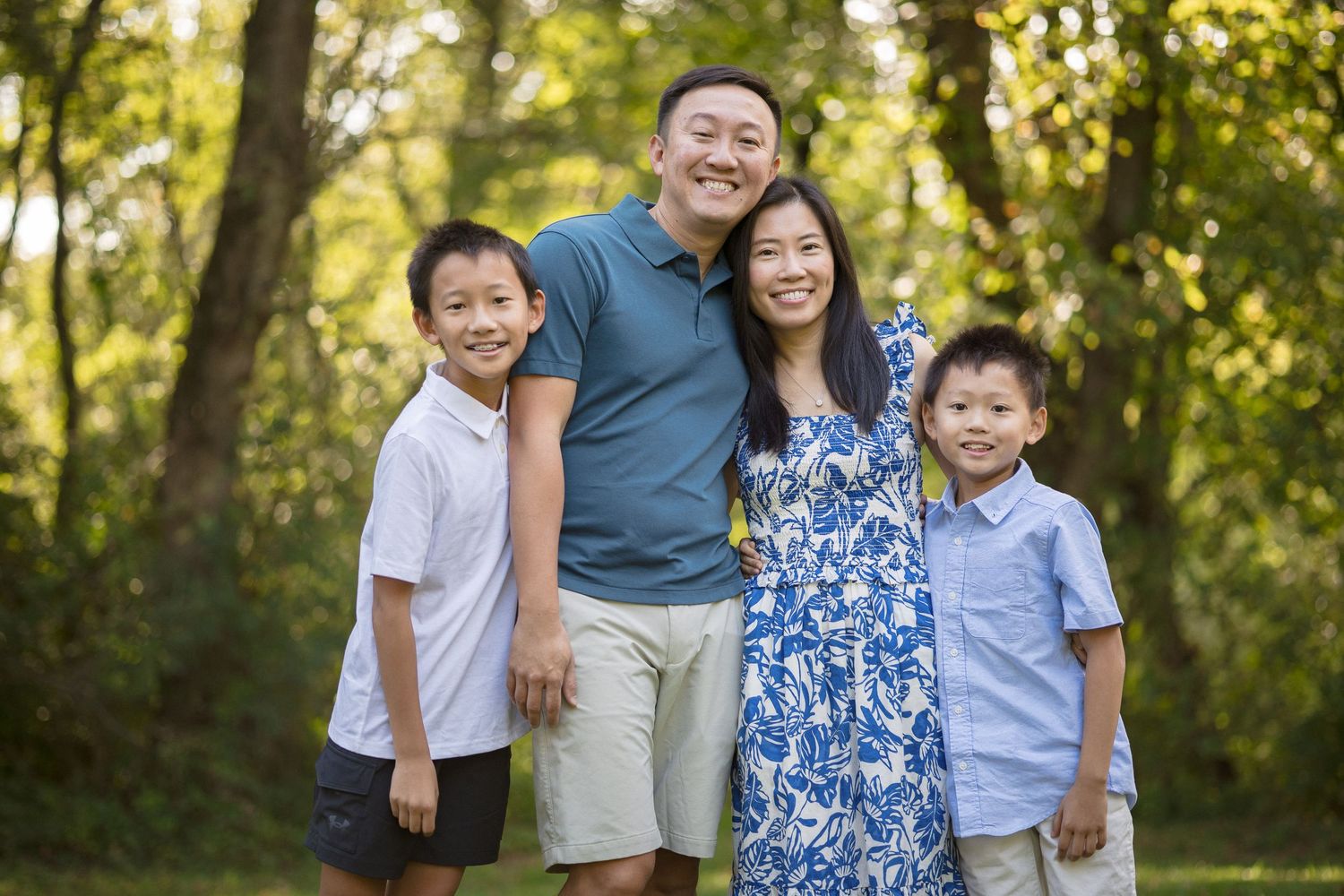 Happy Asian family of four smiling outdoors in a lush green park setting.