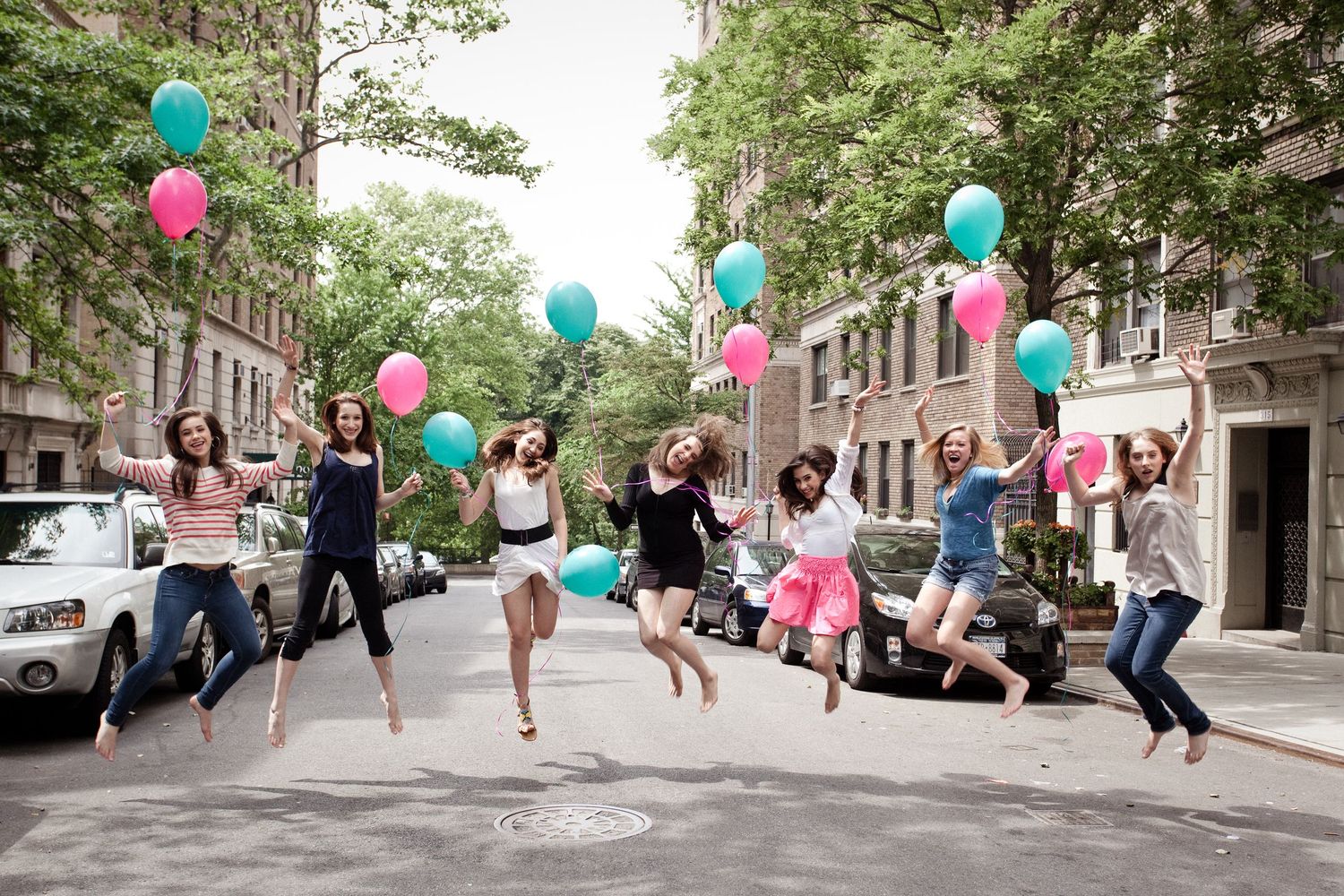 Group of women jumping joyfully on a city street holding colorful balloons.