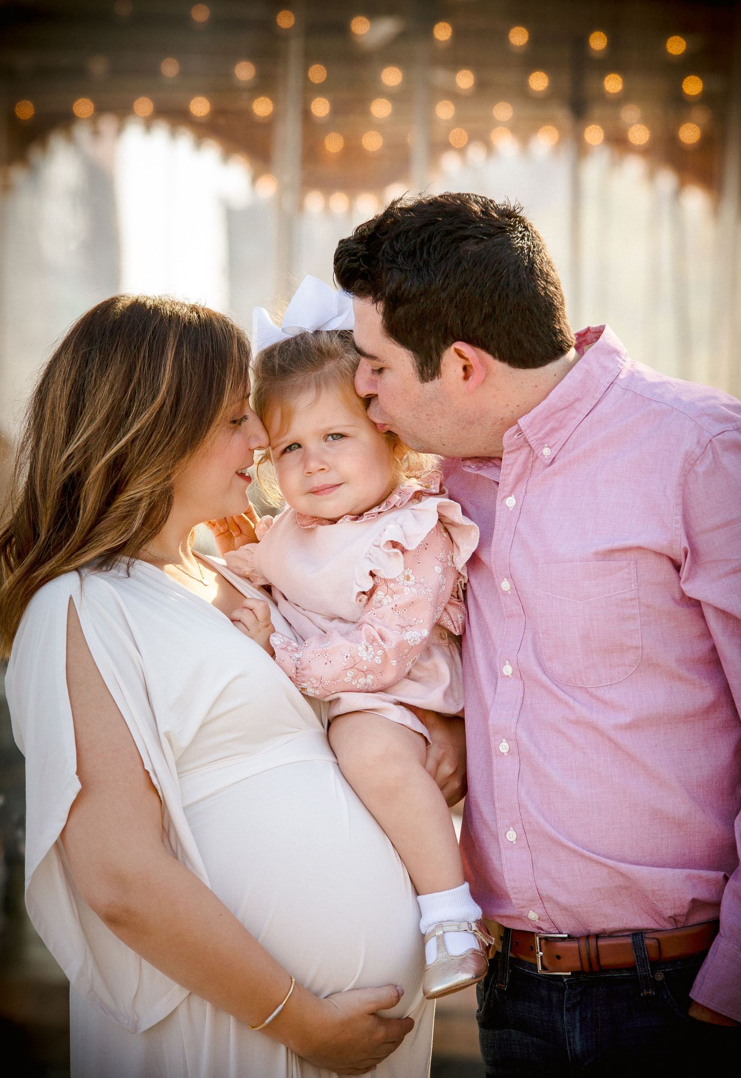 Pregnant couple kissing toddler daughter in maternity photo.