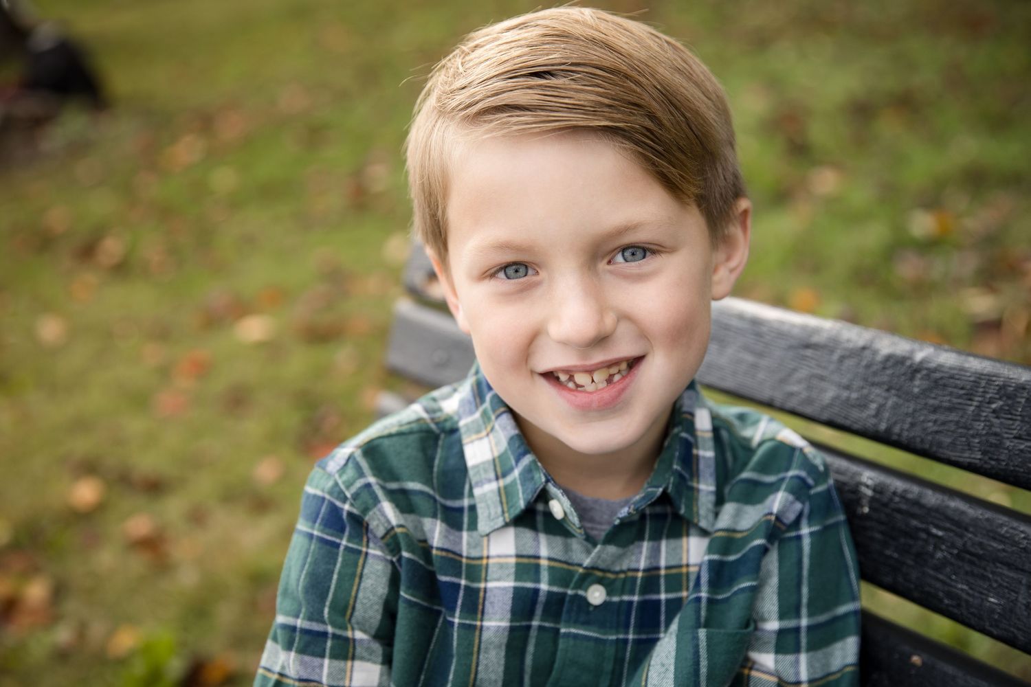 Happy freckled boy with blonde hair smiling on a wooden park bench in autumn.