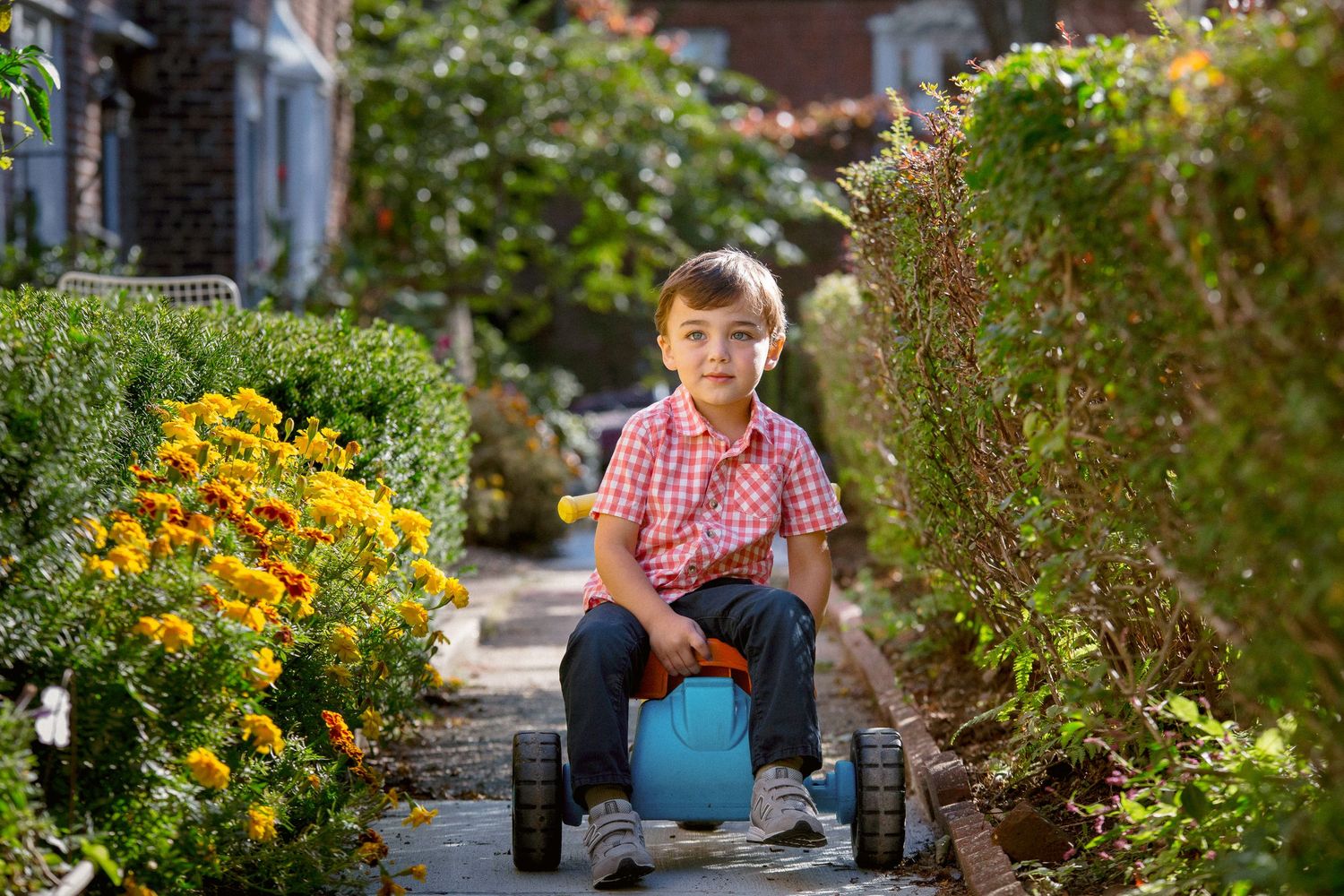 Young boy sitting on blue ride-on toy in a garden pathway.