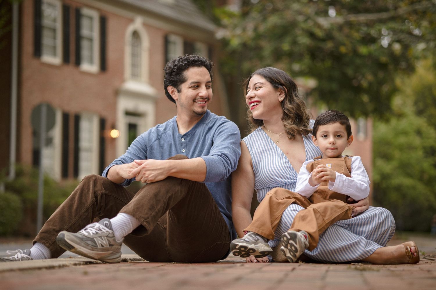 Happy family of three sitting on brick steps outside a historic brick home, smiling and enjoying time together.