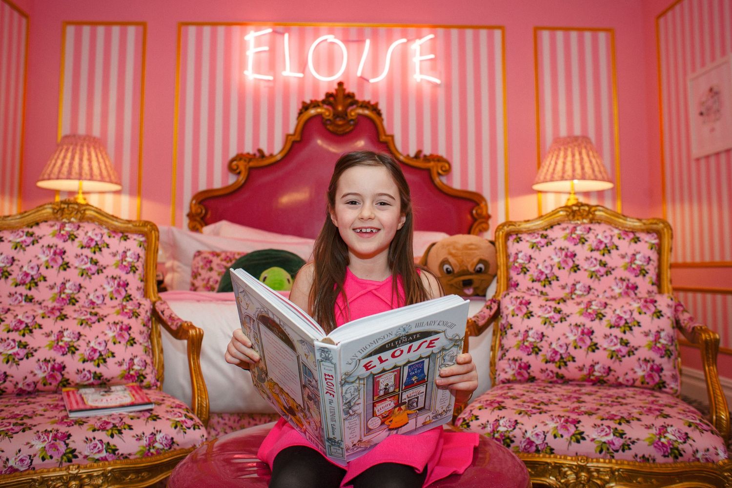 Young girl reading Eloise book in pink themed Eloise suite at The Plaza Hotel.