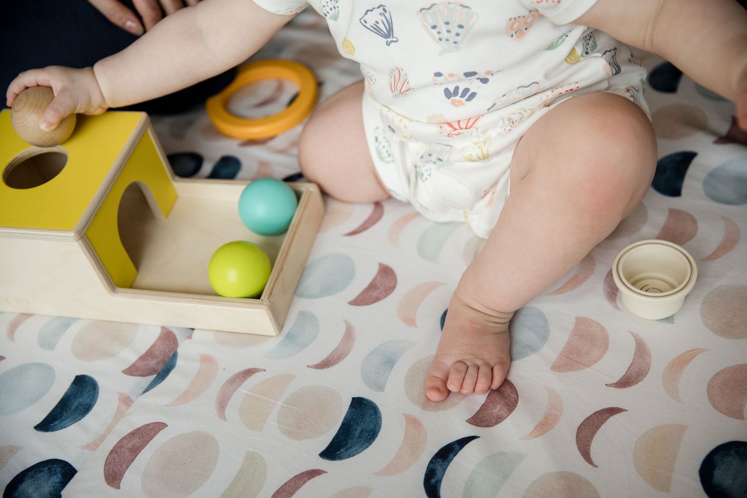 Baby in diaper playing with colorful Montessori wooden toy balls on a patterned play mat.