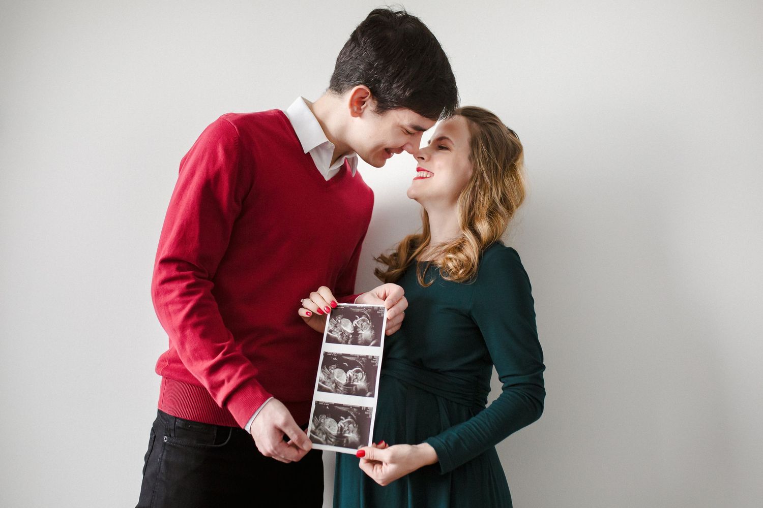 Young couple touching foreheads while holding ultrasound photos during a maternity announcement session.