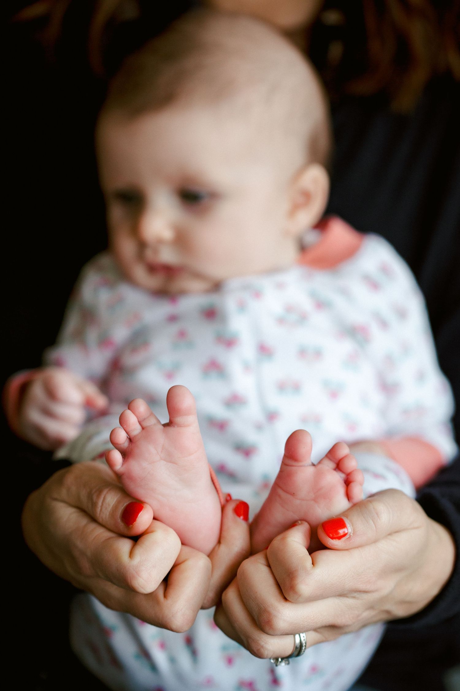 Mother with red nails gently holds her baby's tiny feet in focus in the foreground.