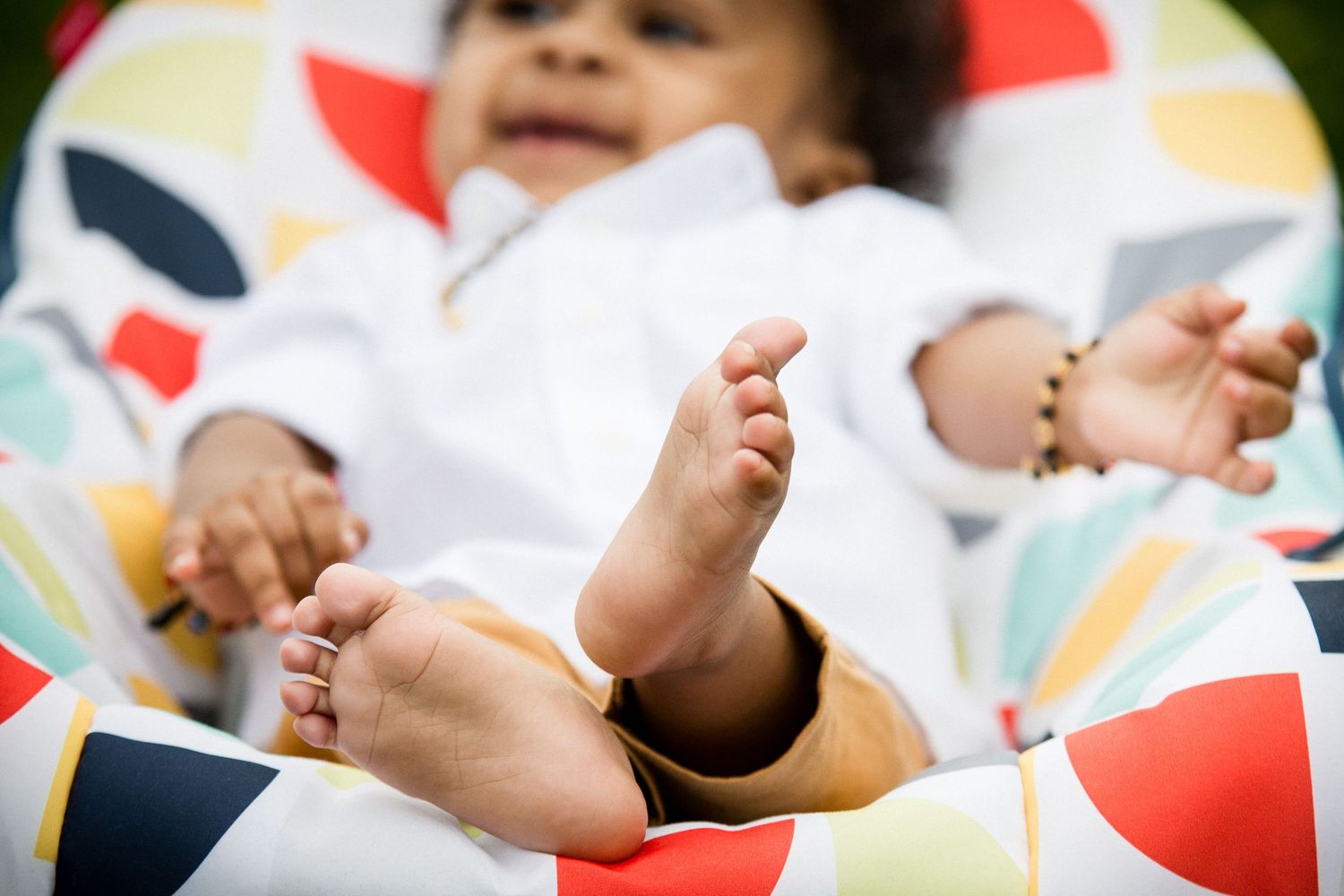 Close-up of baby feet with colorful patterned blanket while infant relaxes outdoors.