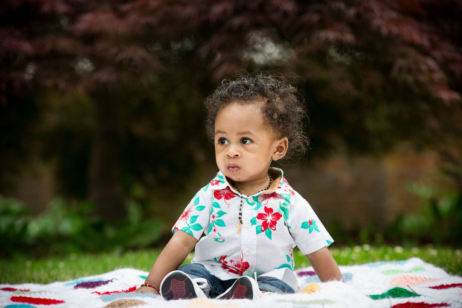 Adorable toddler in floral outfit sitting on blanket in garden.