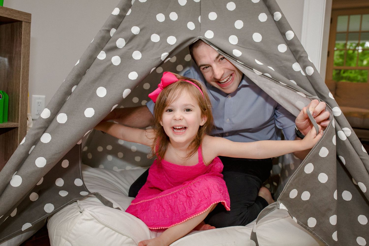 Father and daughter smiling inside a gray polka dot play tent.