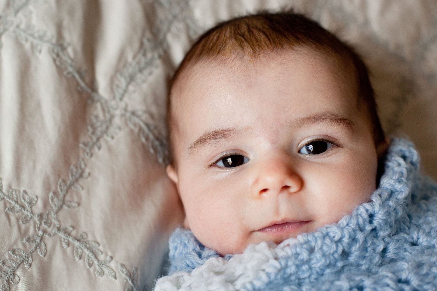 Sweet newborn baby wrapped in a soft blue blanket lying on a quilted white surface.