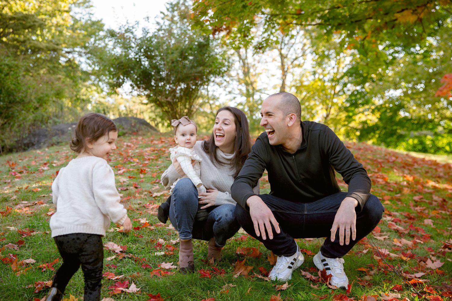 Happy family with two young daughters laughing together in autumn park with colorful foliage.