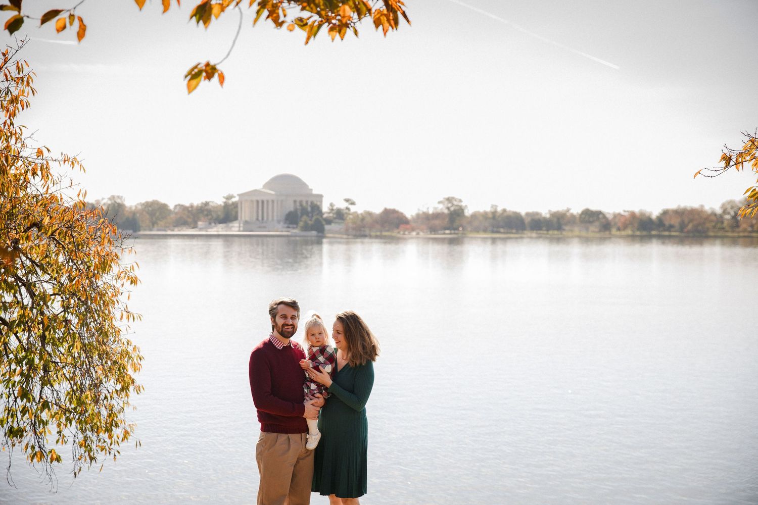Young family with baby poses by the Tidal Basin with Jefferson Memorial backdrop.