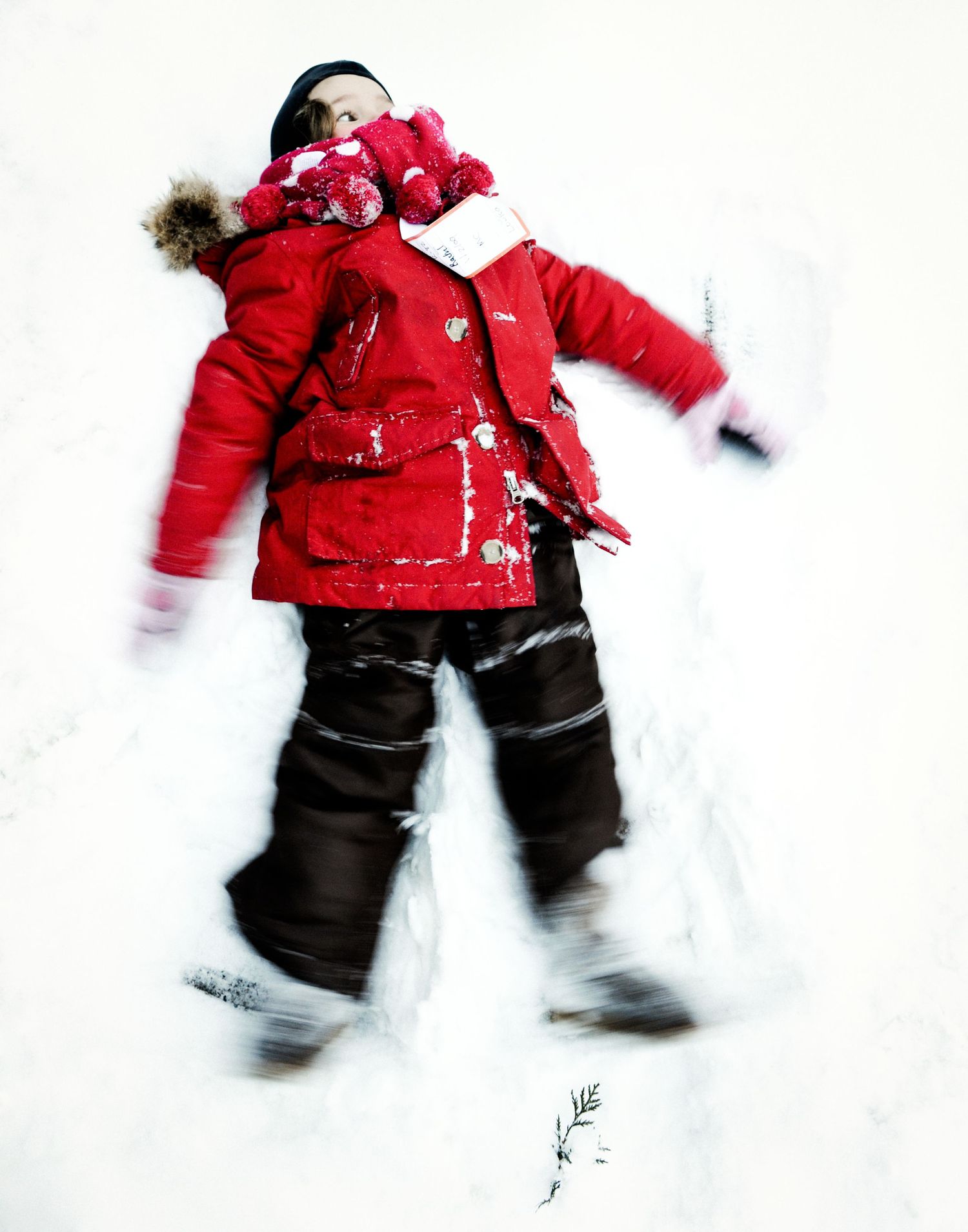 Child in red winter jacket making a snow angel in fresh white snow outdoors.
