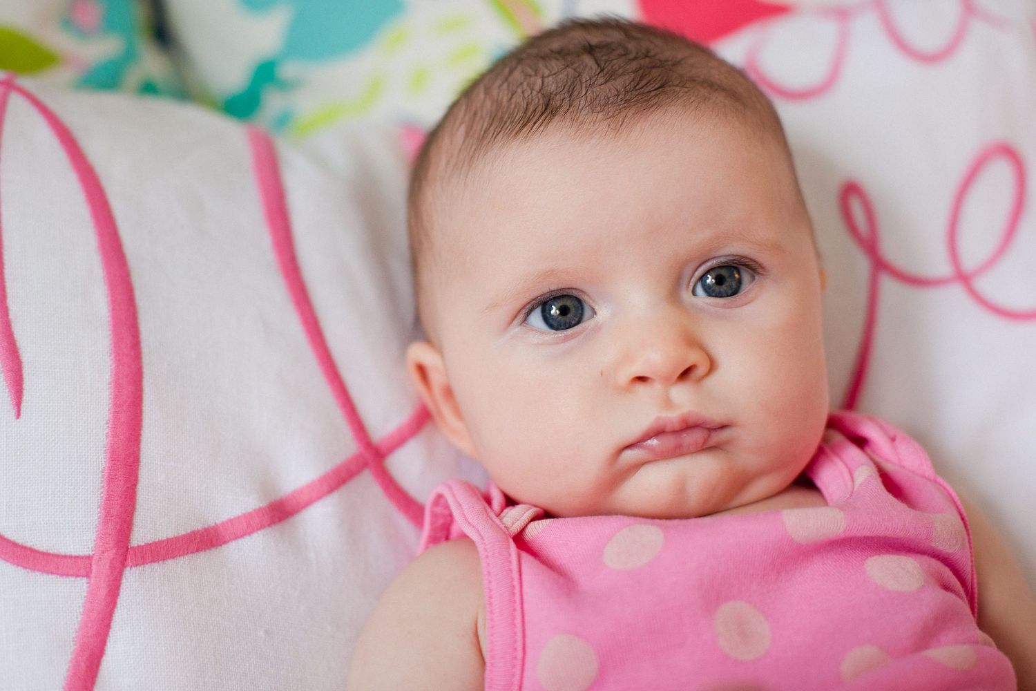 Close-up portrait of cute blue-eyed baby girl in pink polka dot outfit.