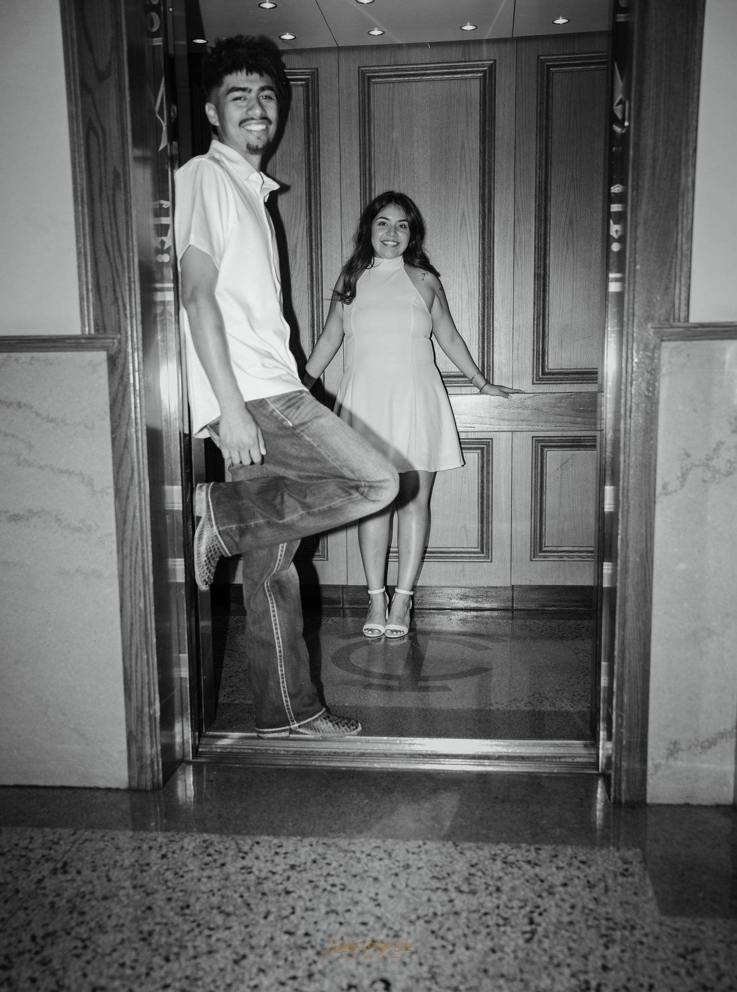Black and white photo of a smiling couple posing playfully in an elegant doorway.