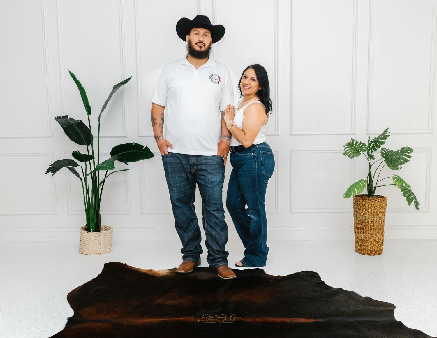 Couple posing together in casual white shirts and jeans on a cowhide rug.