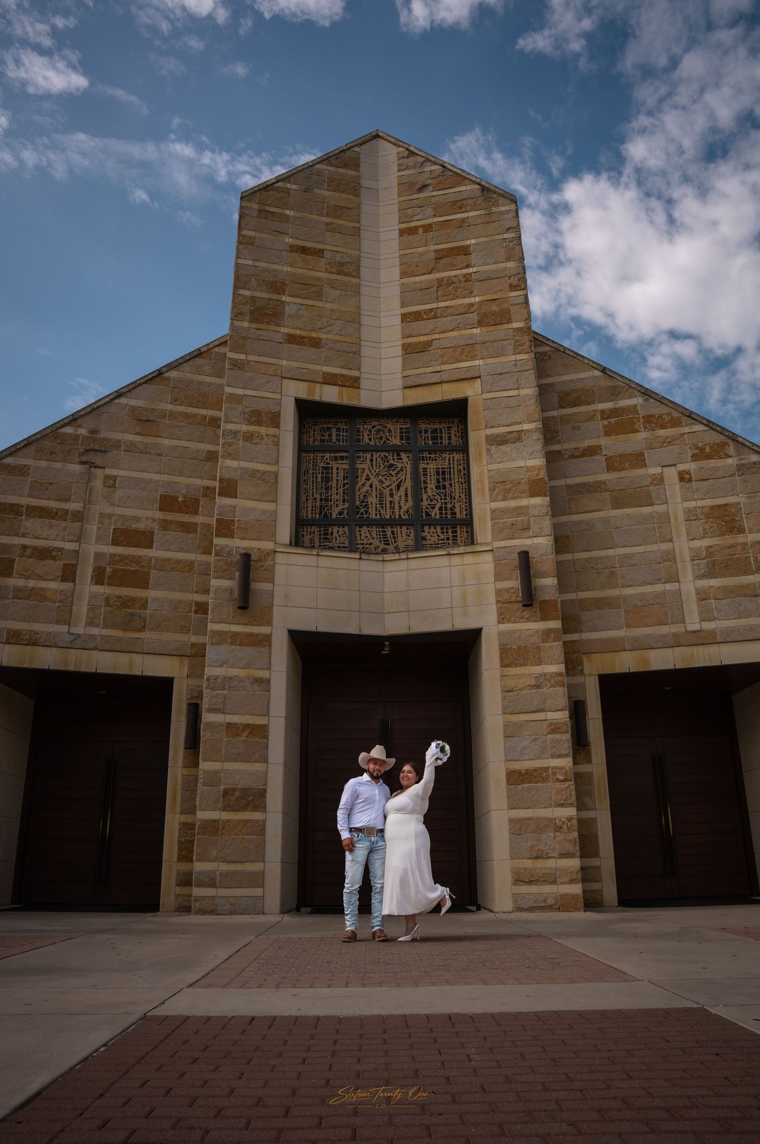 Couple dancing joyfully in front of a large stone church under a blue sky.