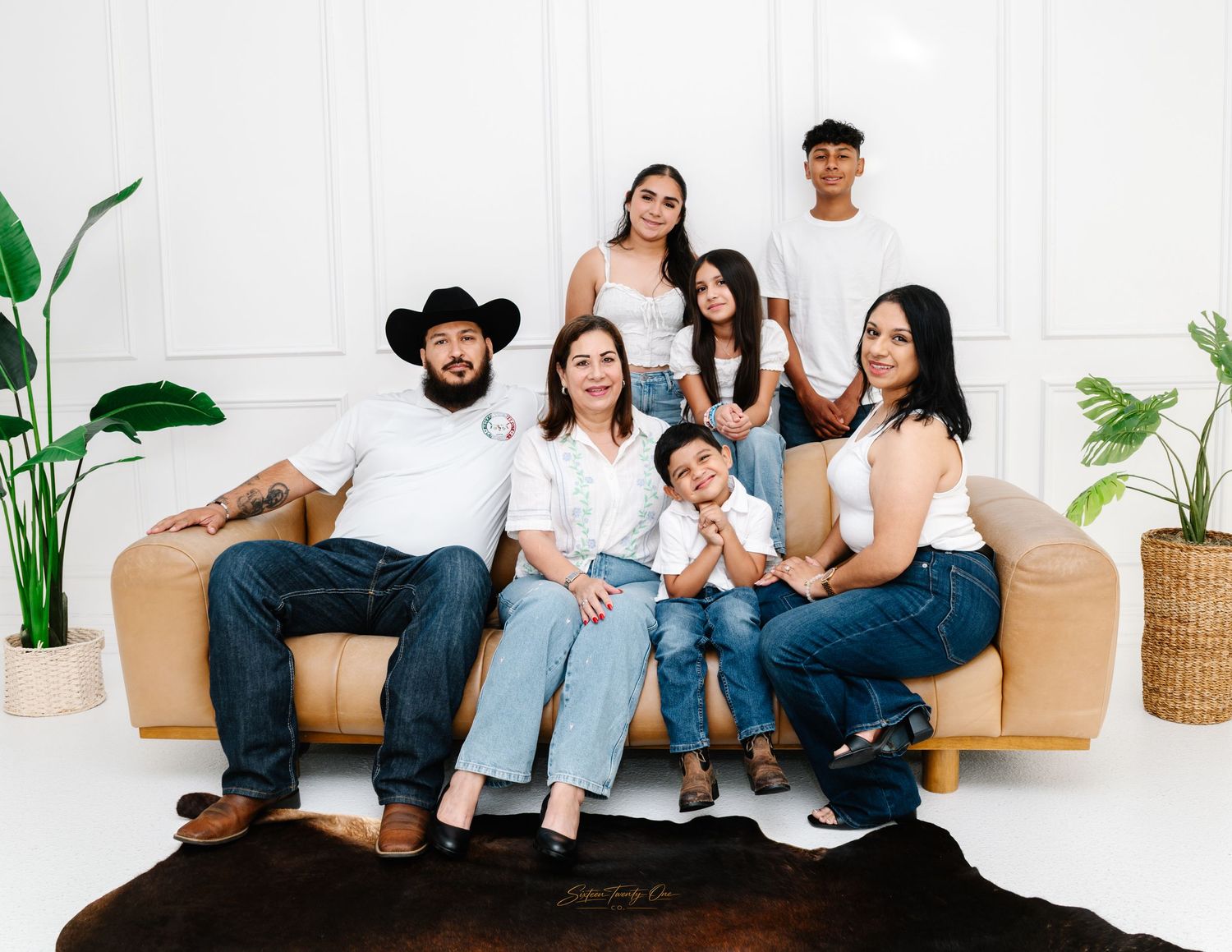 Large Hispanic family posing together on a couch in a bright white studio setting.