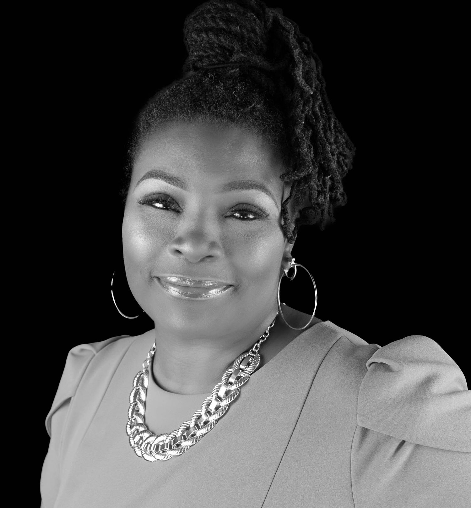Professional black and white portrait of a smiling woman wearing hoop earrings and a chunky chain necklace.